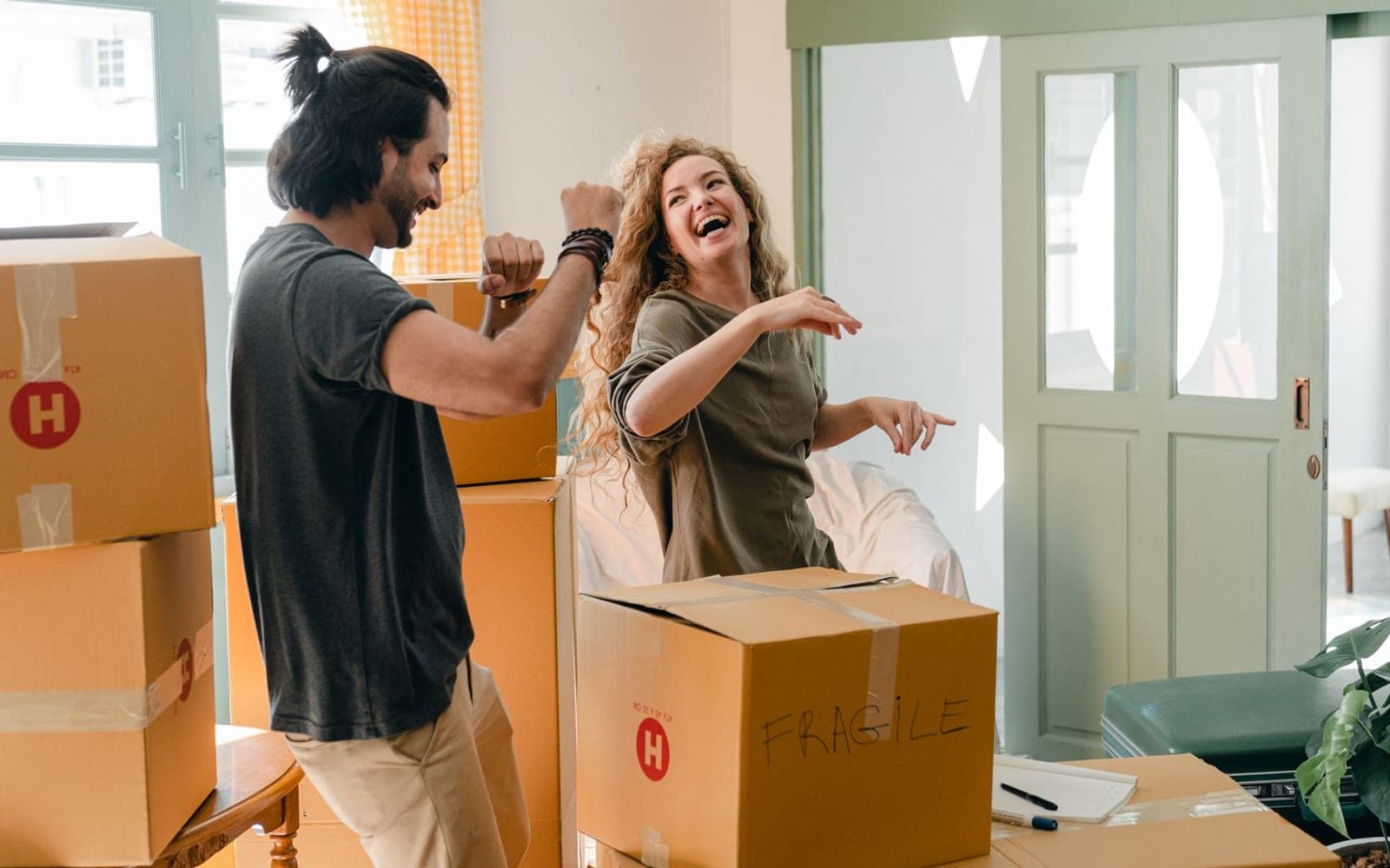 Casal ri enquanto abre caixas de papelão dentro de casa