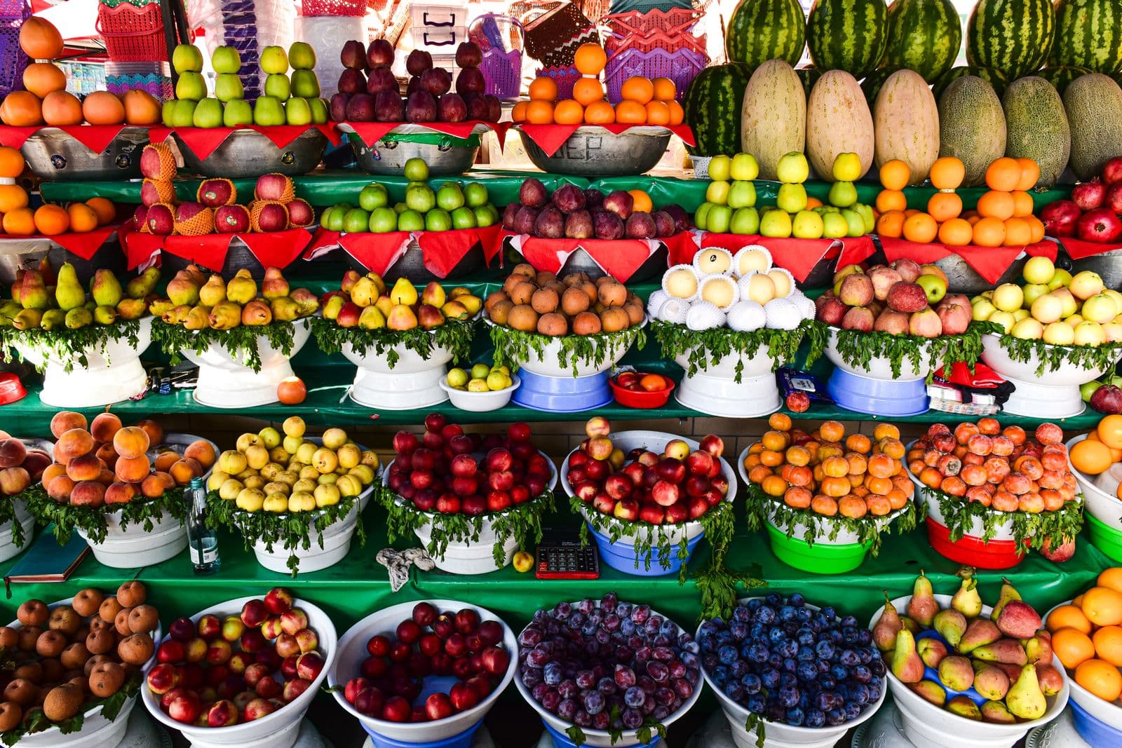 Banca de frutas com maçãs, peras, laranjas, melões e melancias arrumados em fileiras