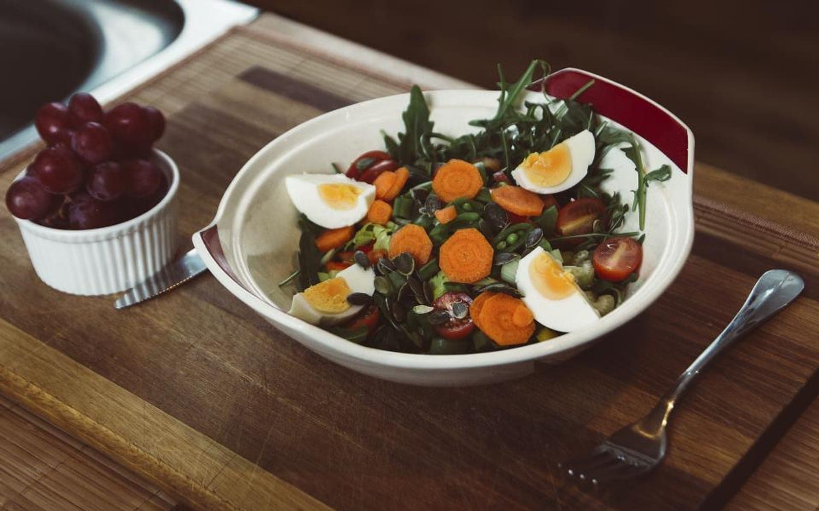 Prato com salada de folhas, ovo cozido e rodelas de cenoura sobre uma bandeja de madeira