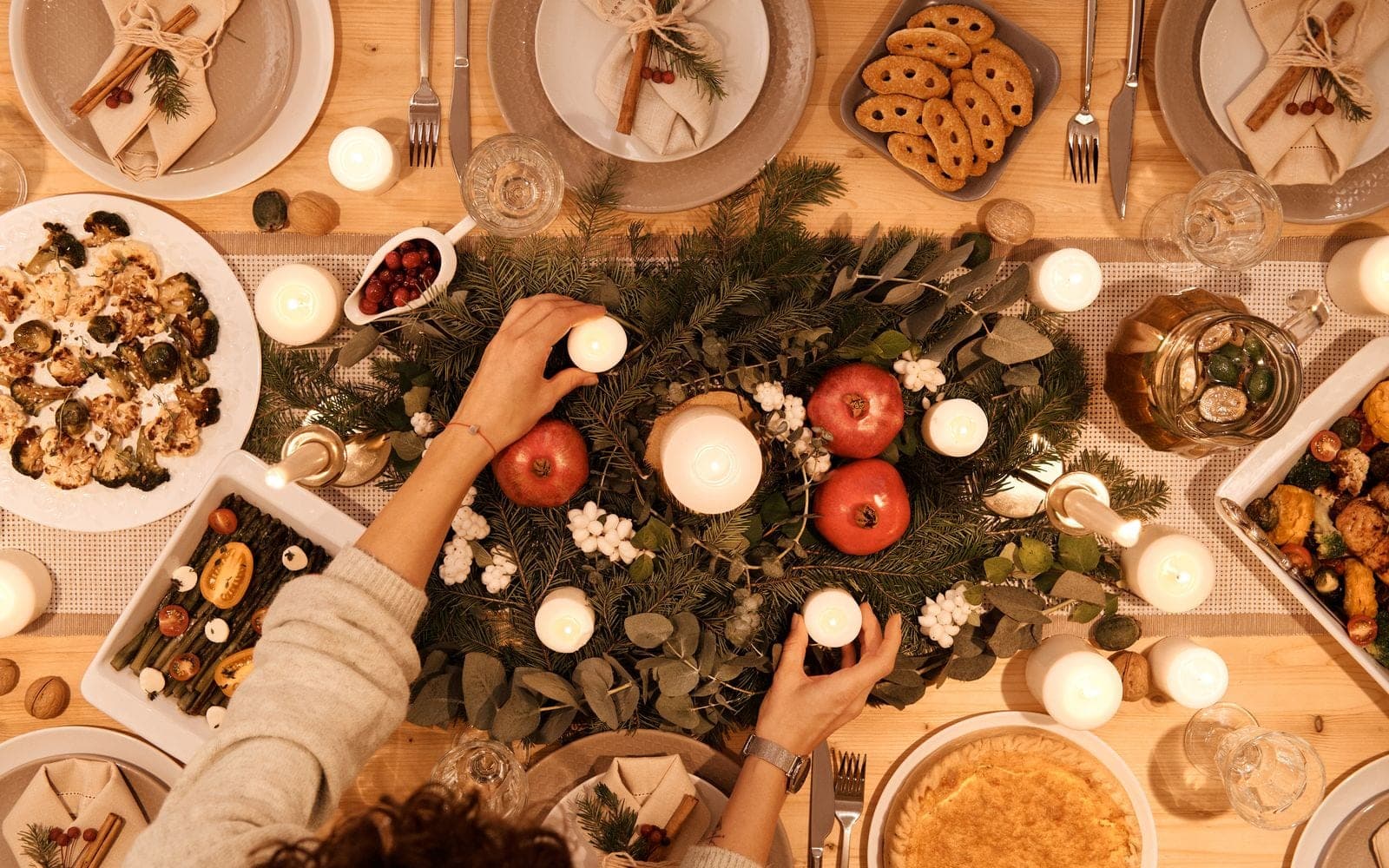Vista de cima de uma mesa de Natal com pratos, velas, vermelhos e um arranjo de folhagens