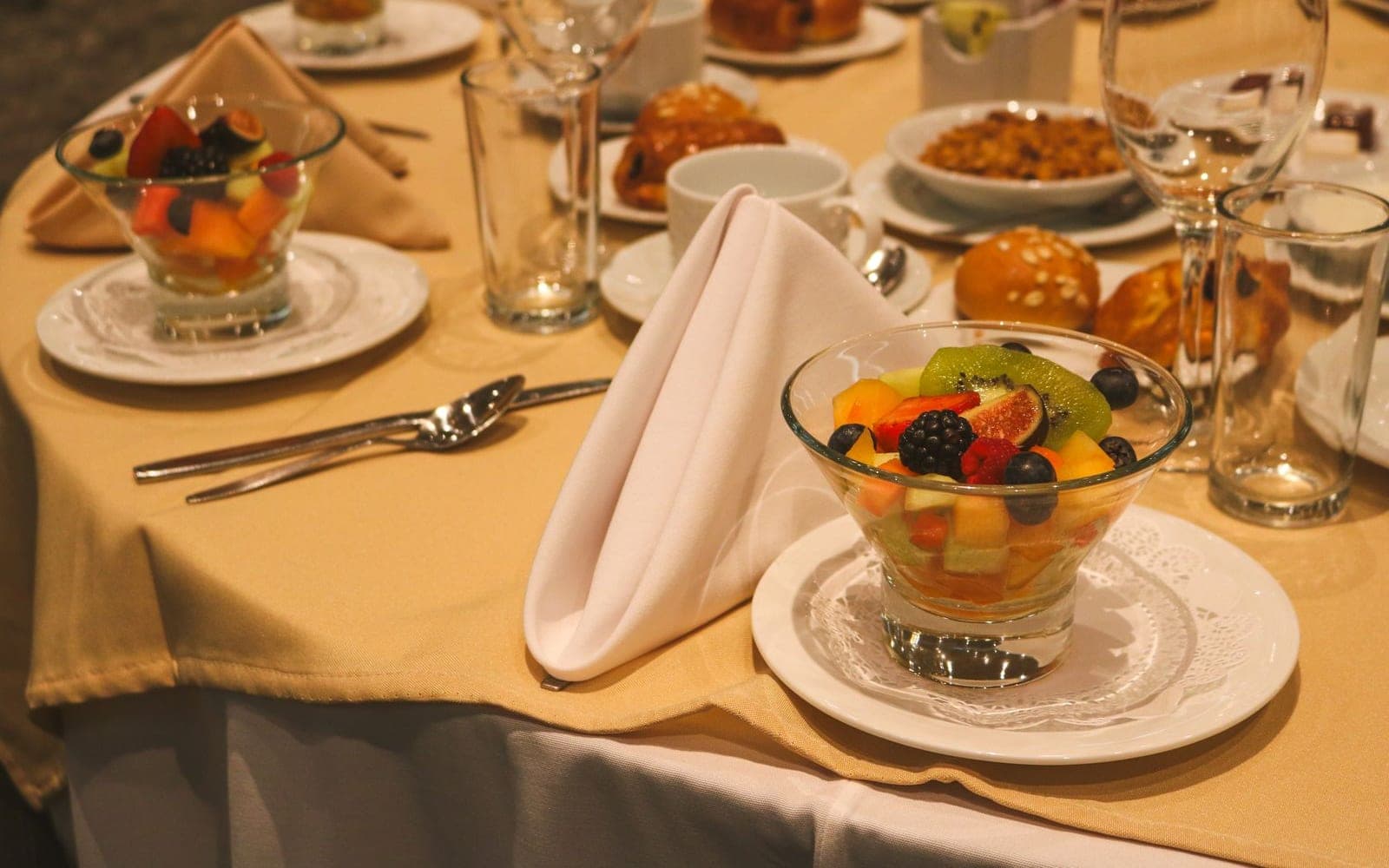 Mesa posta com taças de salada de frutas coloridas, guardanapo e talheres