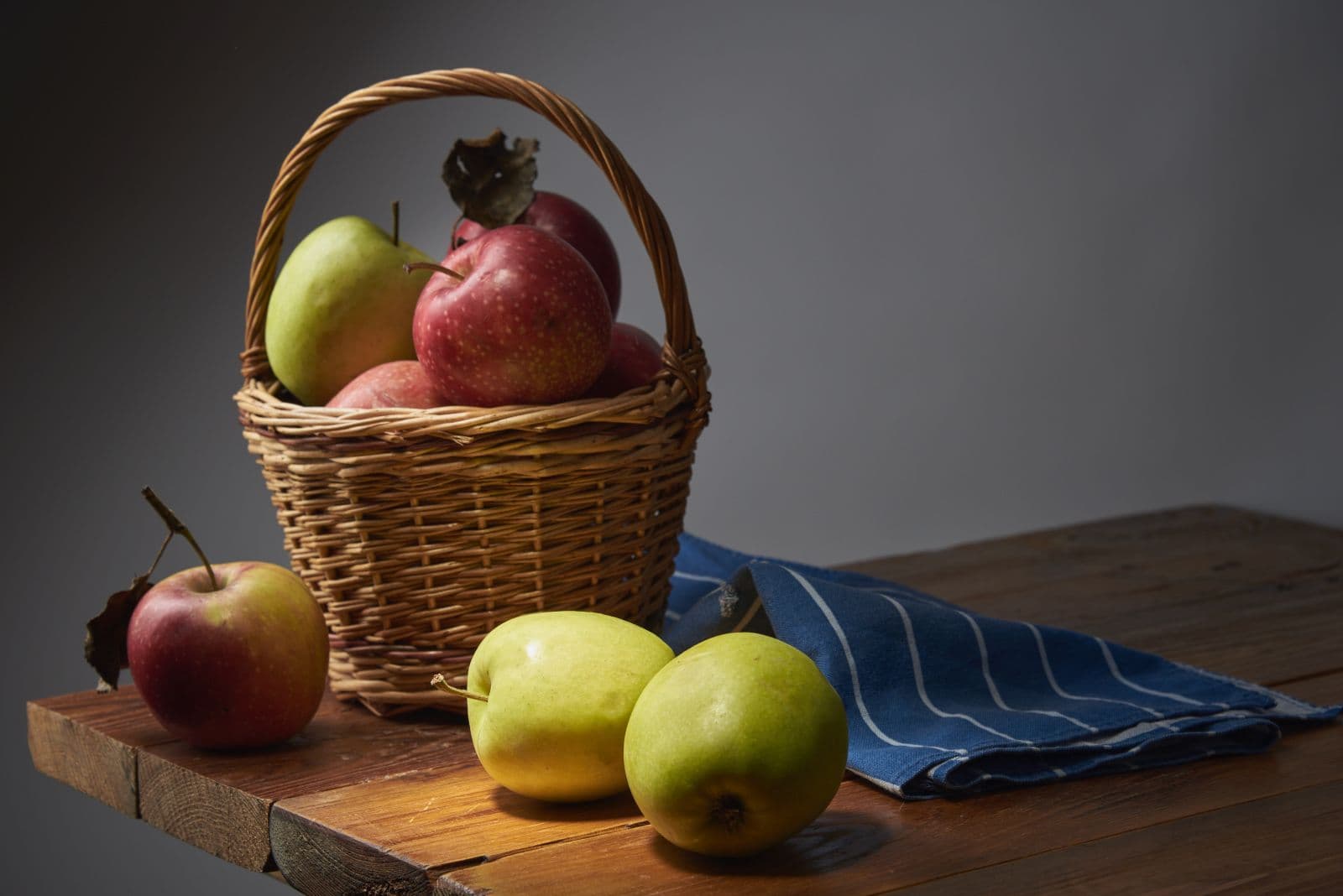 Cesta de vime com maçãs vermelhas e verdes sobre mesa de madeira