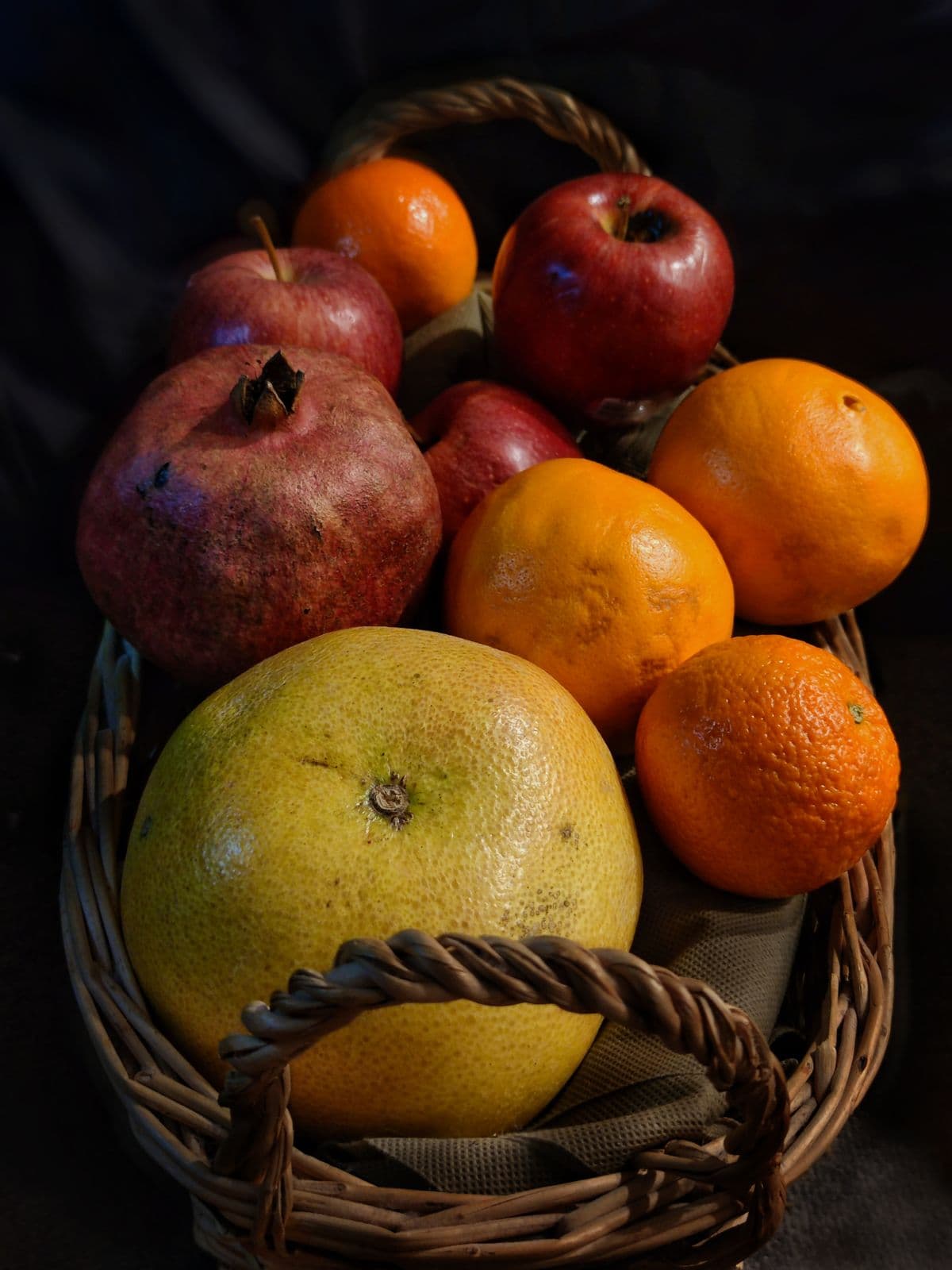 Cesta de vime com romãs, maçãs, laranjas e toranja