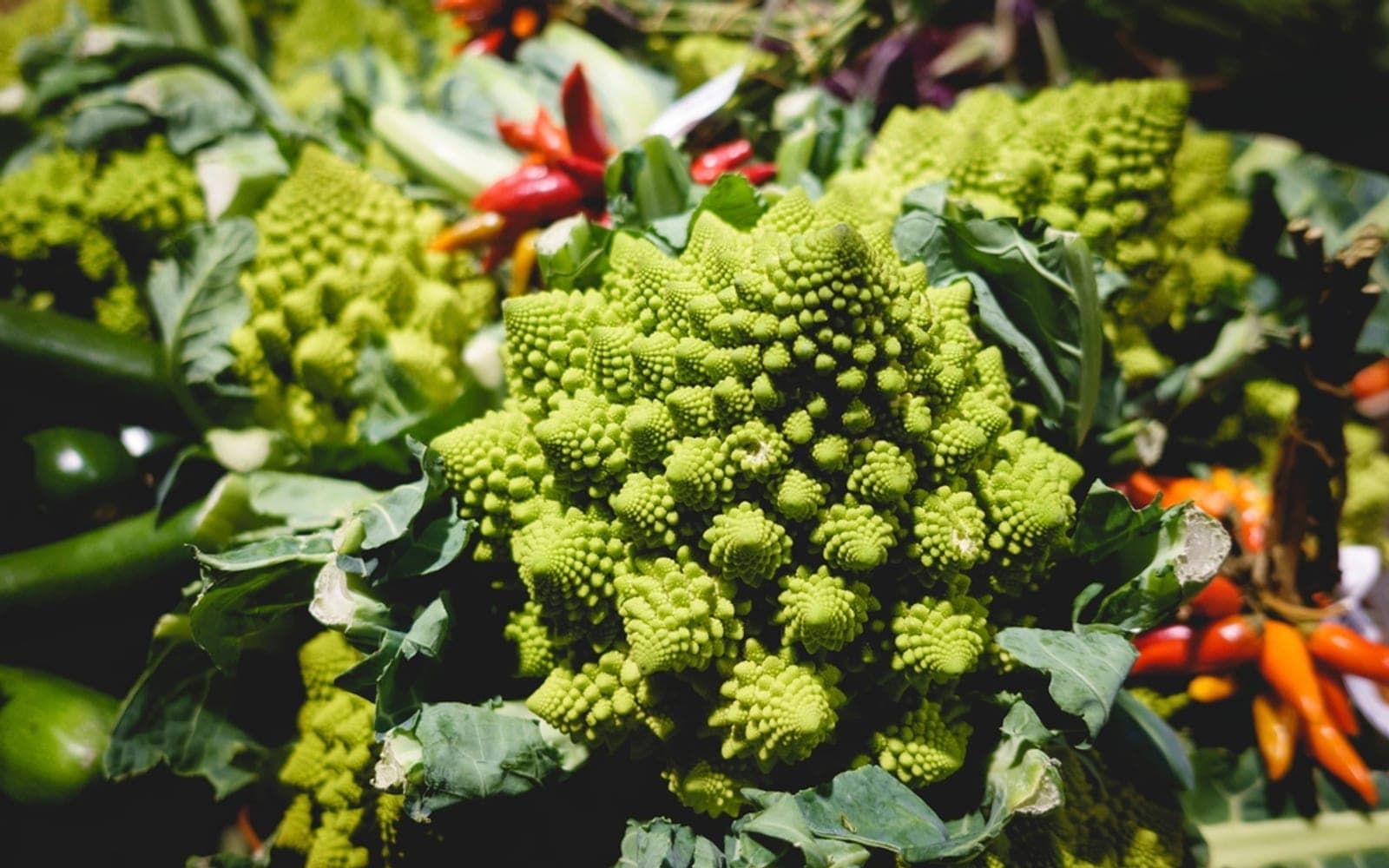 Couve-romanesco verde ao lado de pimentas vermelhas em uma banca