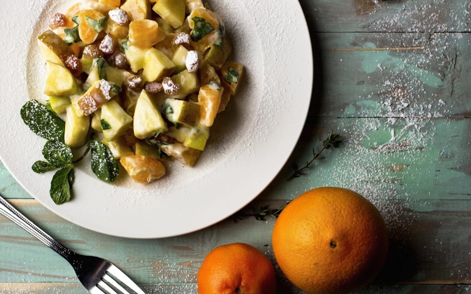 Prato com salada de frutas servida com folhas de hortelã sobre uma mesa rústica