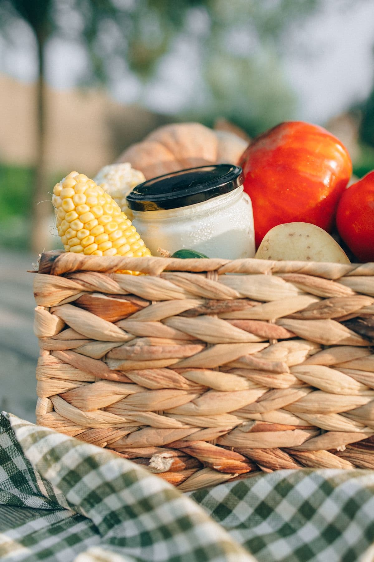 Cesta de vime com milho, tomates e outros vegetais frescos