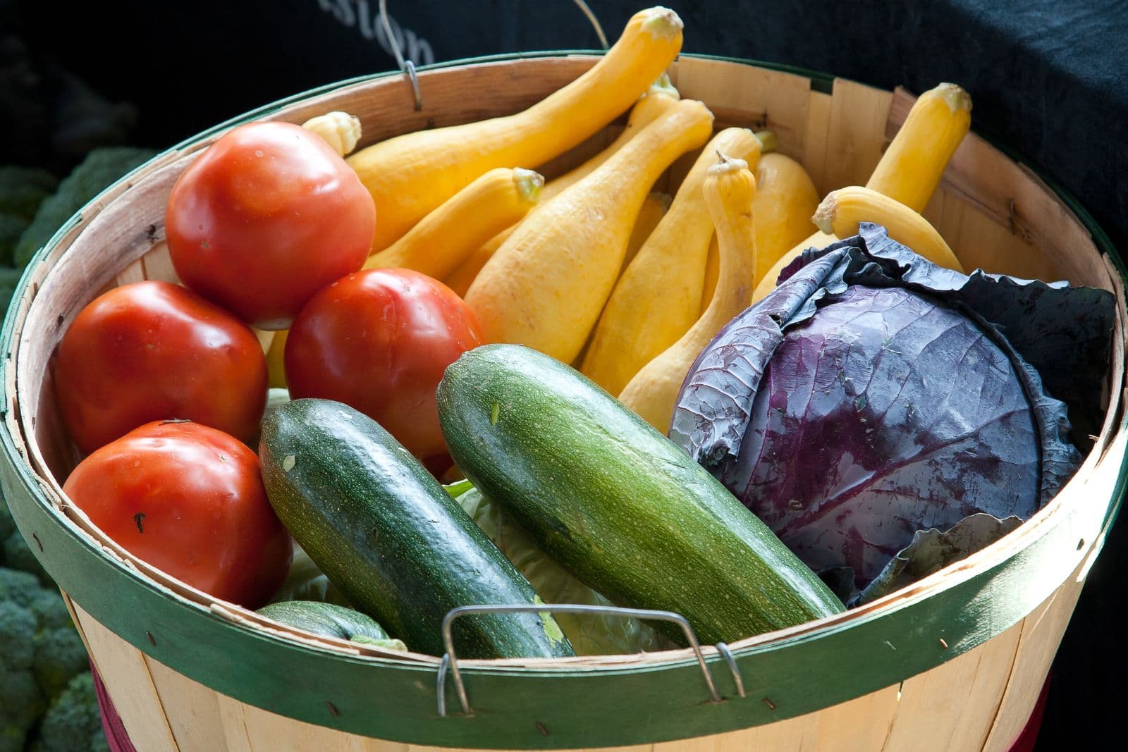 Cesta de vime cheia de tomates, abobrinhas amarelas e repolho roxo frescos