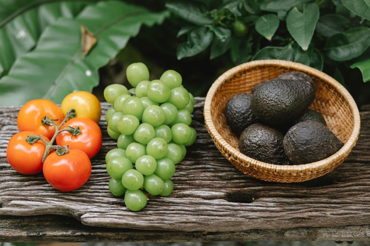 Tomates frescos, uvas verdes e abacates em tigela de madeira