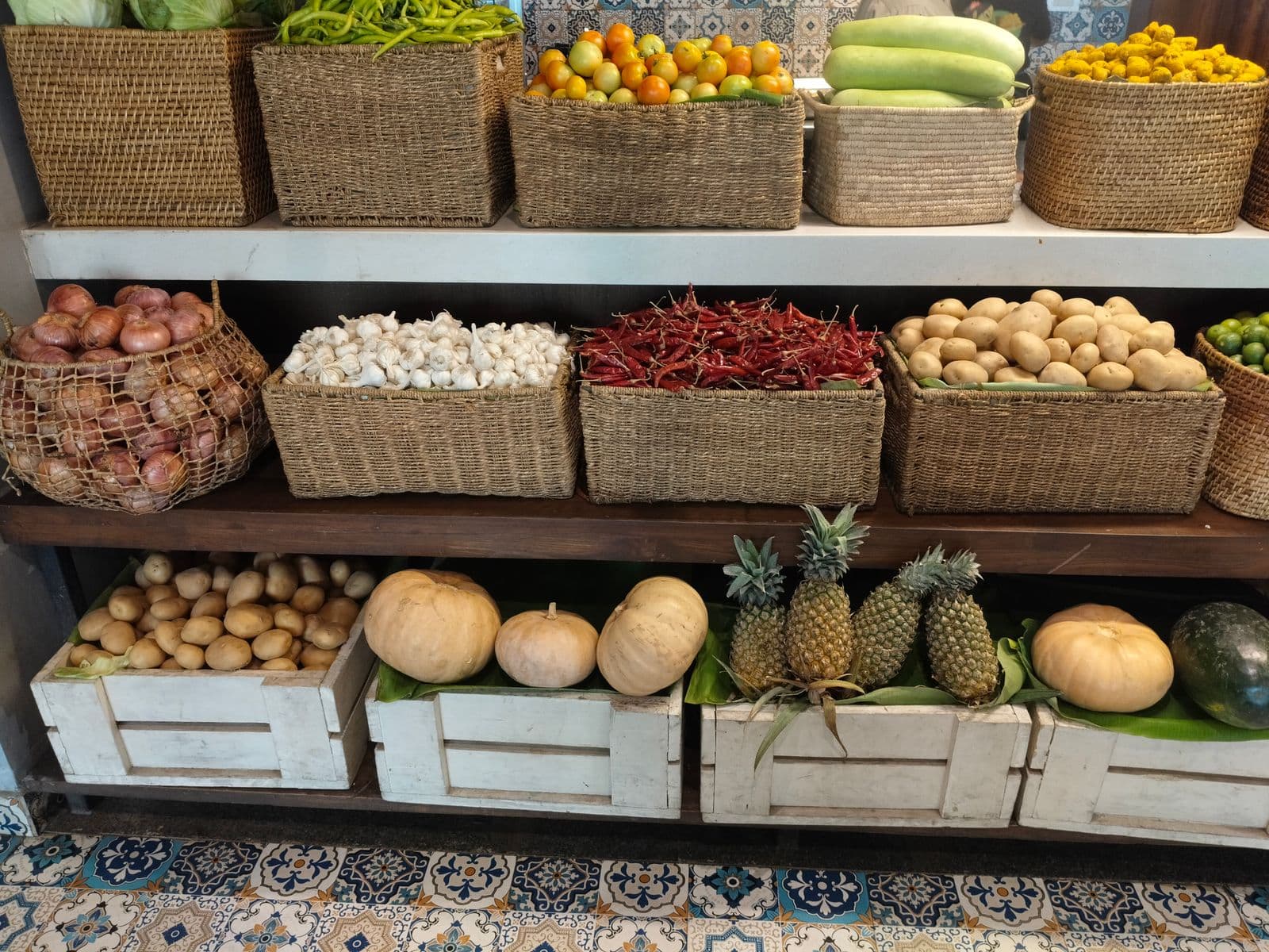 Prateleiras com cestas de vime cheias de legumes, cebolas, alho e abacaxis