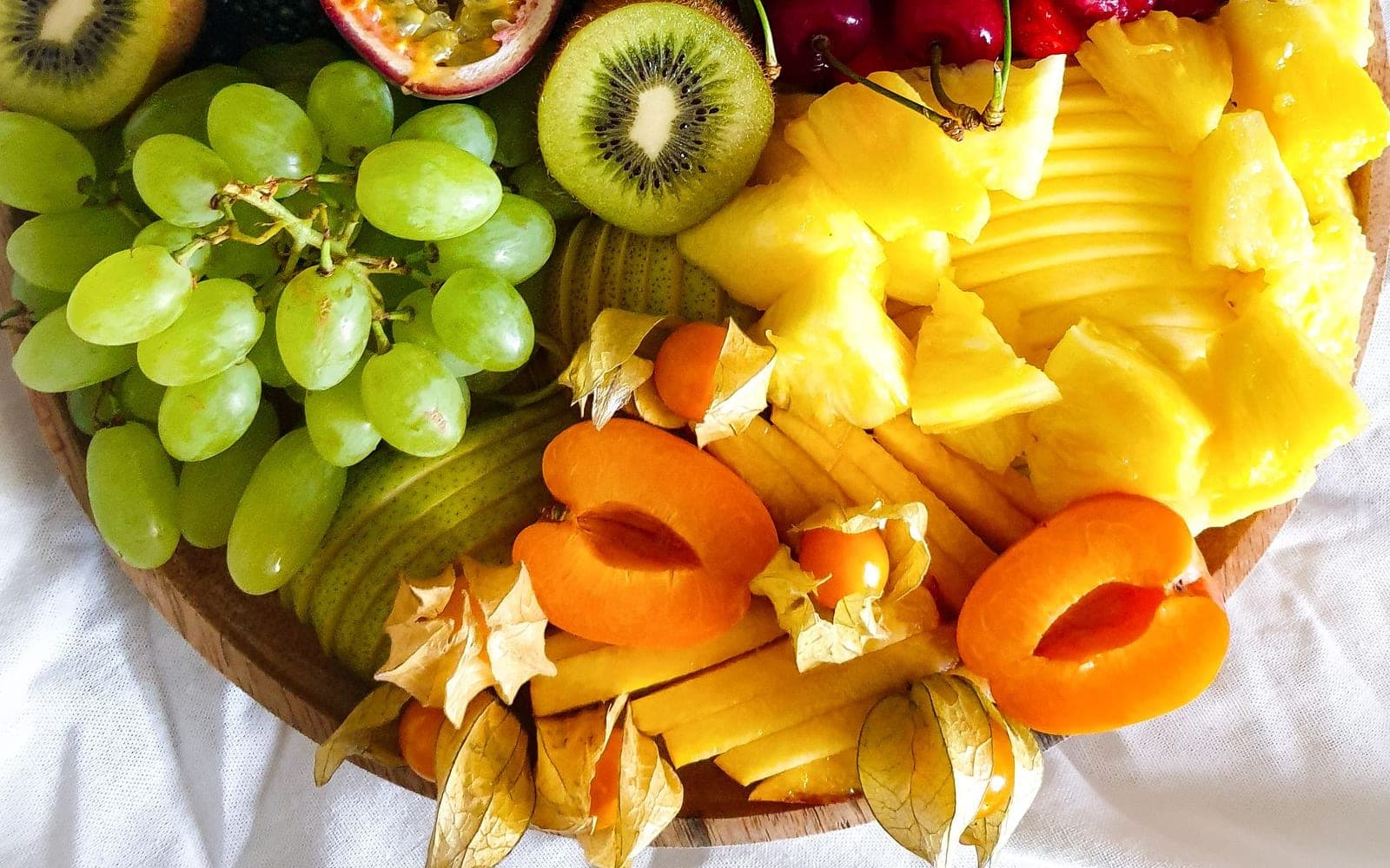 Bandeja com uvas, kiwi, abacaxi, caqui e físalis cortados