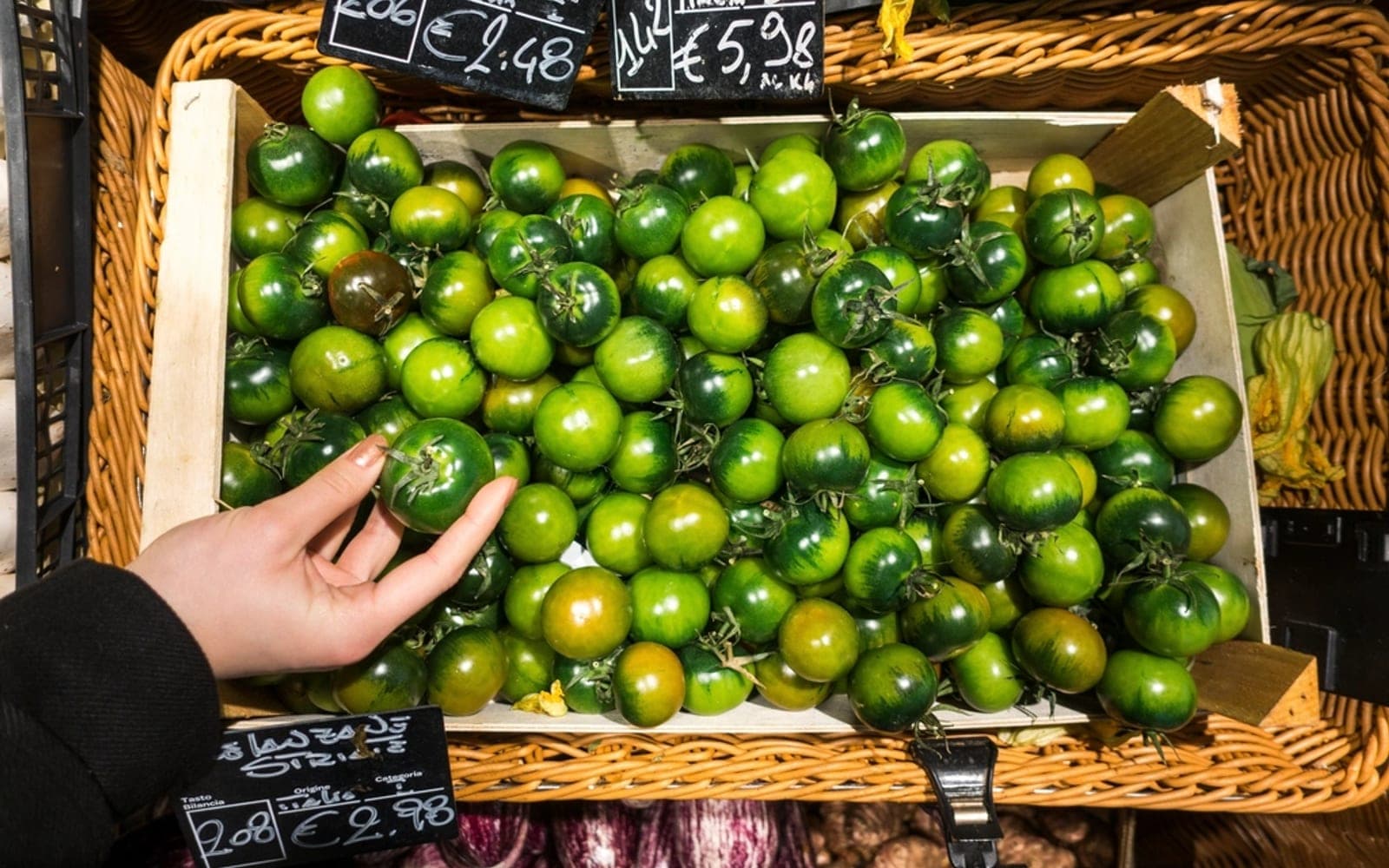 Mão escolhe tomates verdes em uma caixa de madeira de uma banca