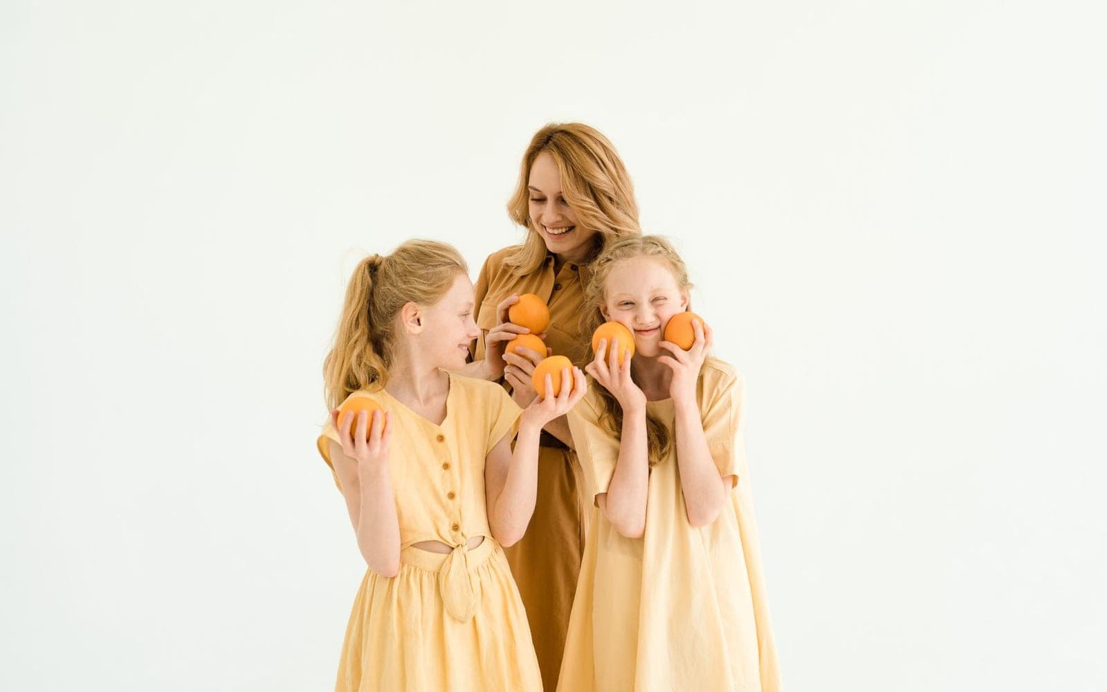 Mãe e duas filhas de vestido amarelo segurando laranjas diante do rosto