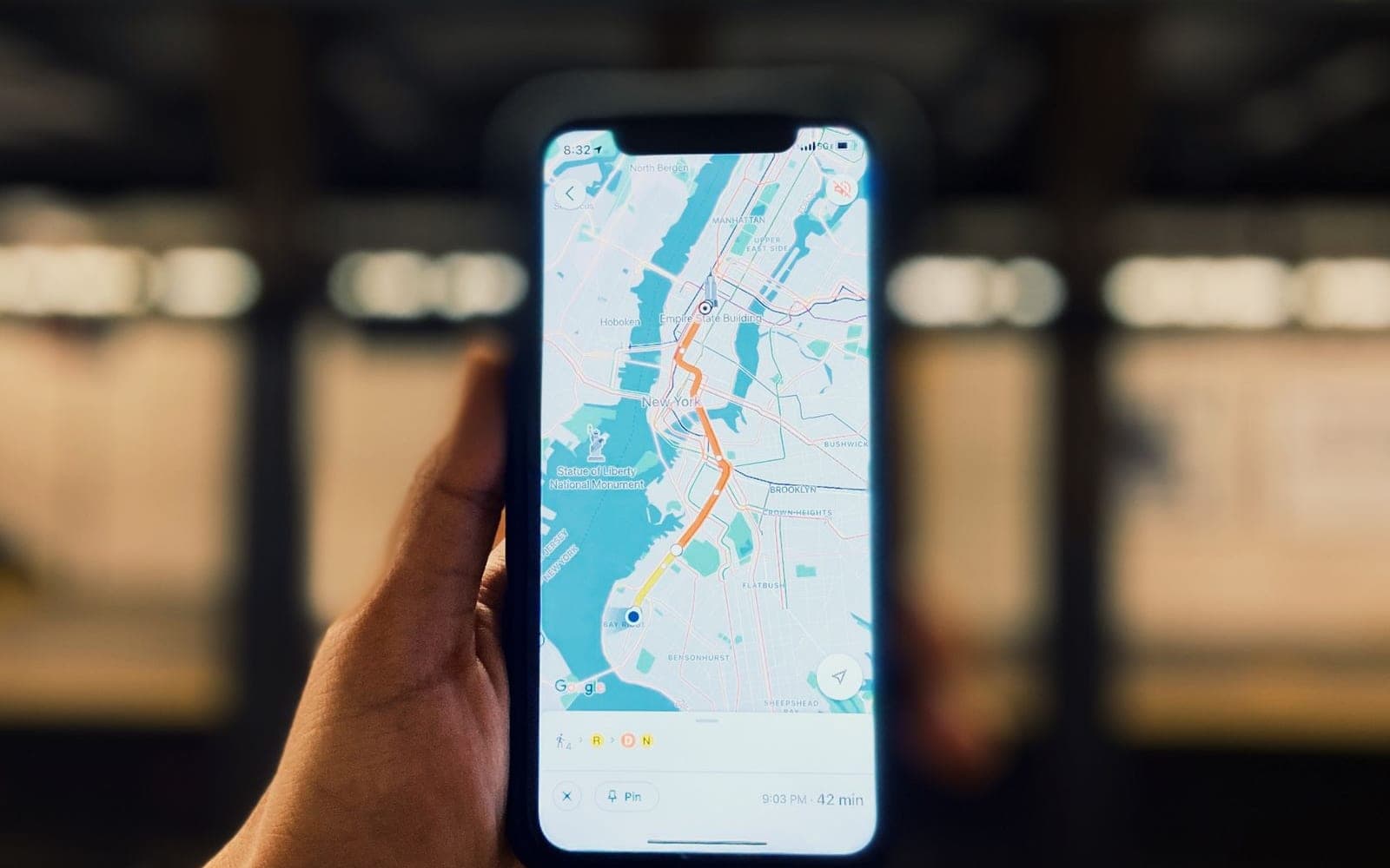 Mão segurando um celular com um mapa aberto, em uma estação