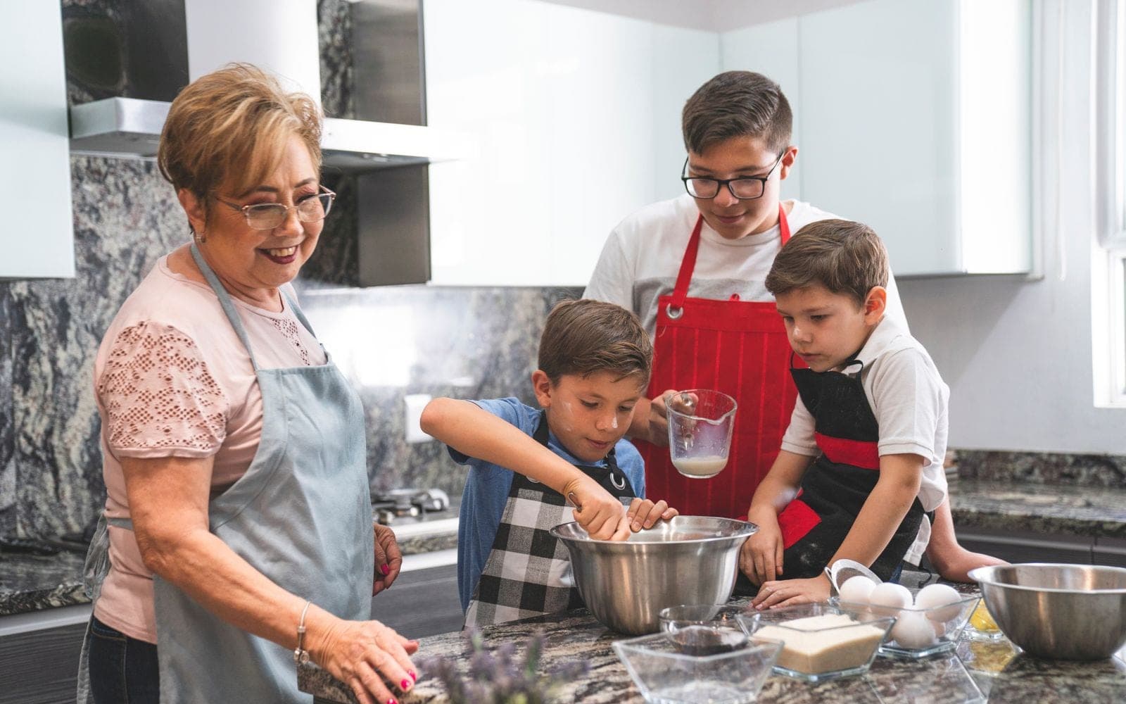Avó, pai e duas crianças de avental cozinham juntos em uma bancada de cozinha