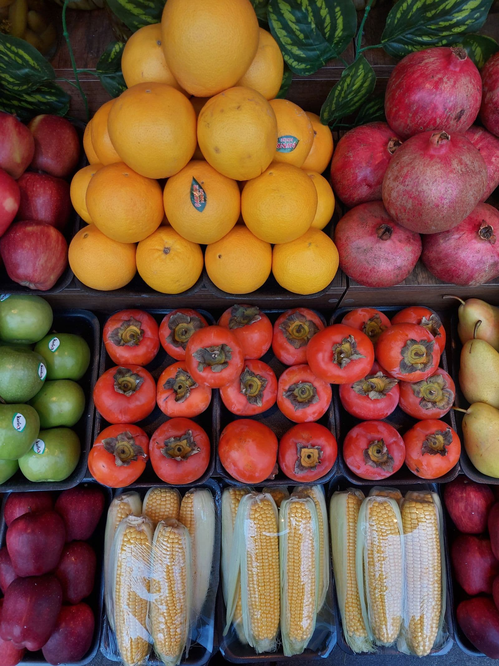 Bancada de feira com laranjas, maçãs, romãs e caquis organizados