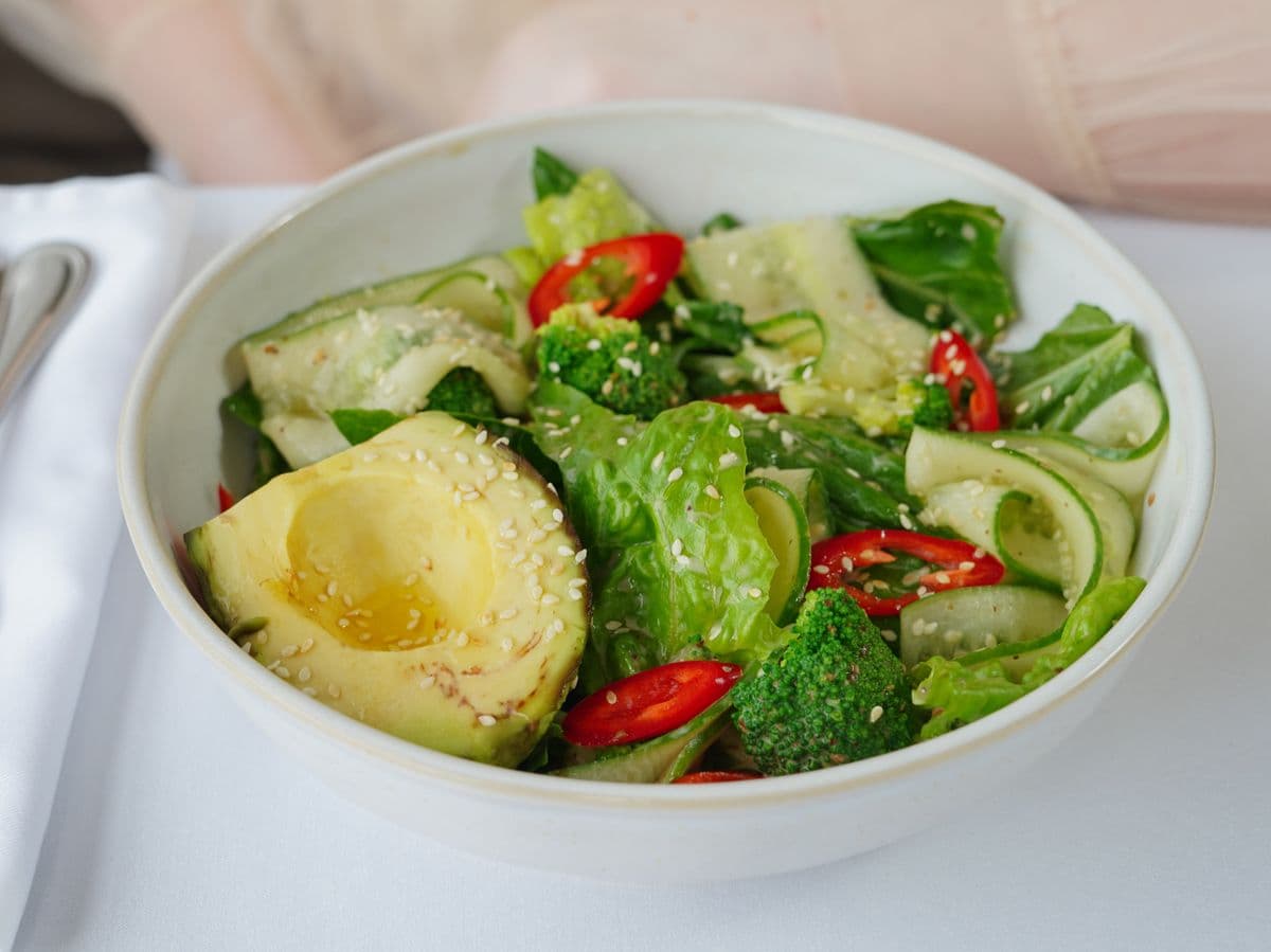 Salada com folhas verdes, brócolis, pepino e abacate em uma tigela branca