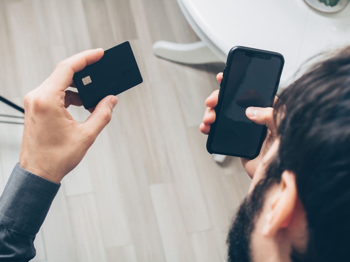 Mão segurando um cartão junto a um celular, vista de cima