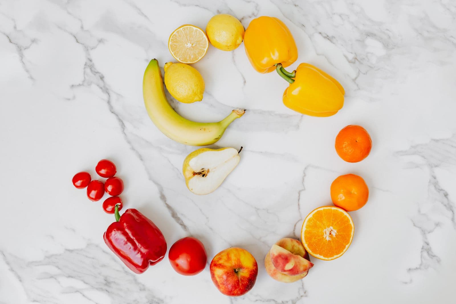 Frutas e verduras de várias cores formando um círculo sobre uma bancada de mármore