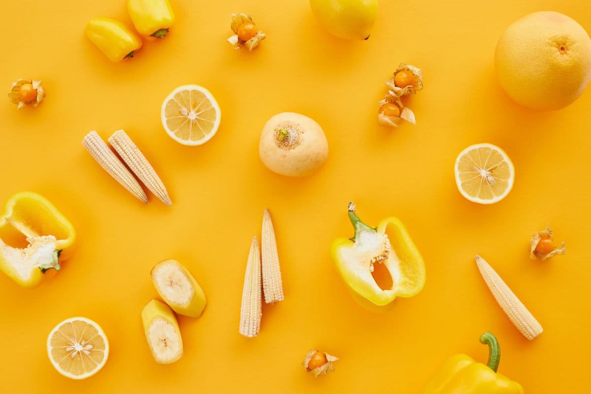 Limões, banana, pimentão amarelo e milho-baby sobre fundo amarelo vibrante