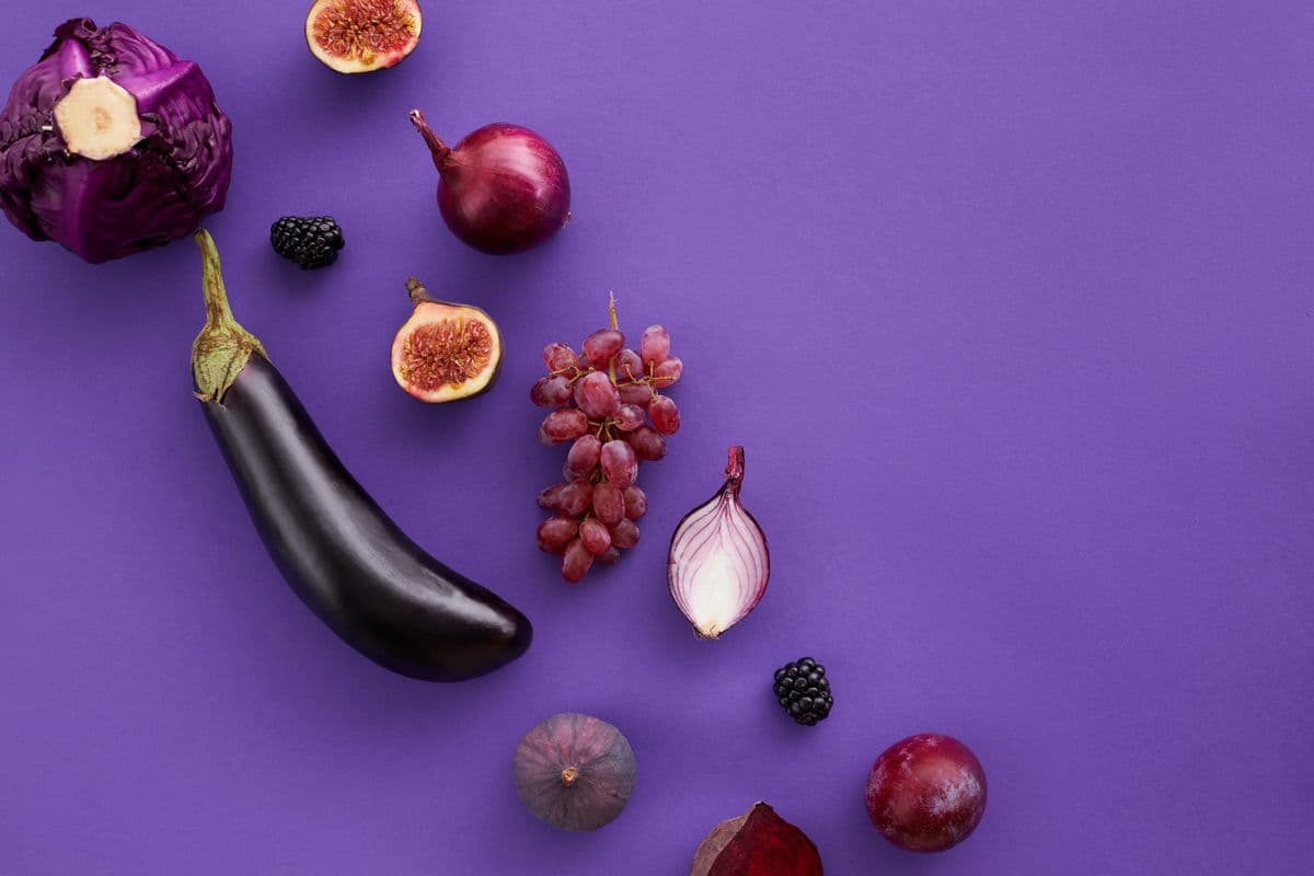 Repolho roxo, berinjela, figos e uvas roxas sobre fundo roxo vibrante