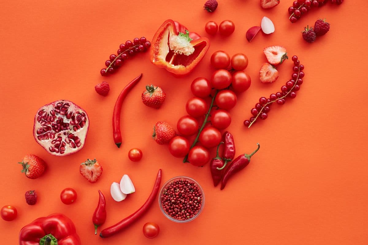 Tomates, morangos, pimentão e romã sobre fundo vermelho vibrante