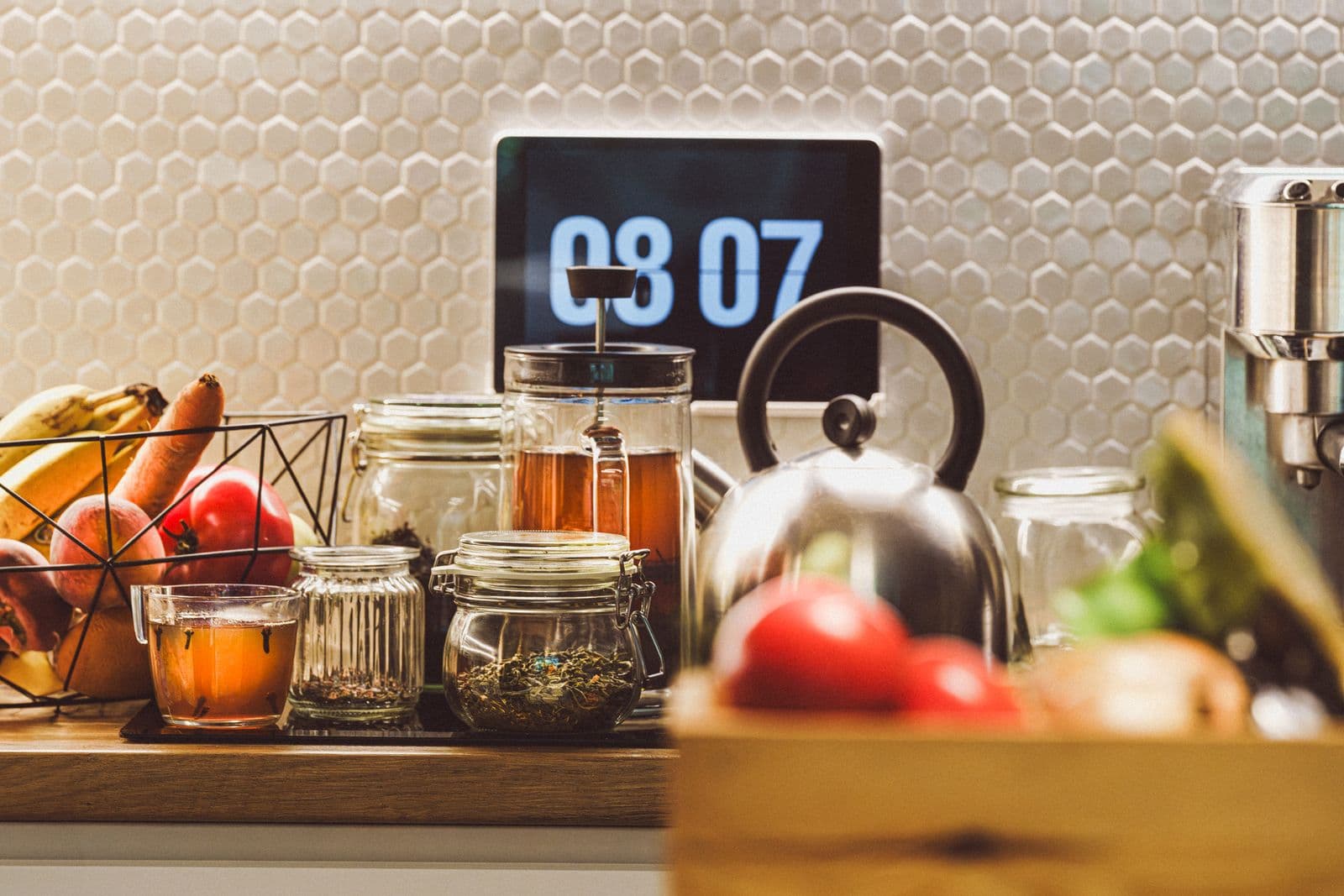 Bancada de cozinha com relógio digital, frutas e potes de chá