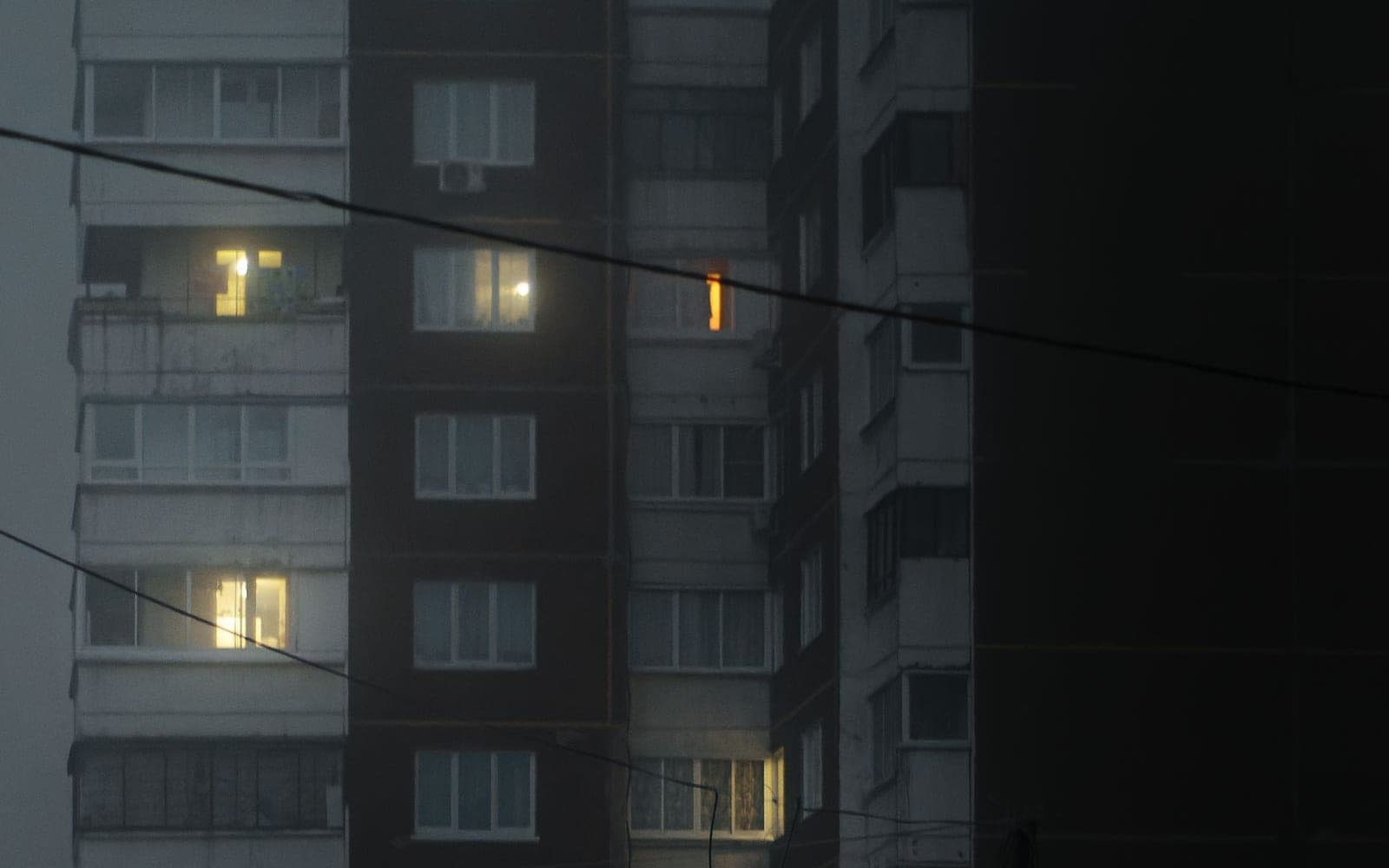 Prédio residencial escuro à noite, com algumas janelas acesas em cinza e azul