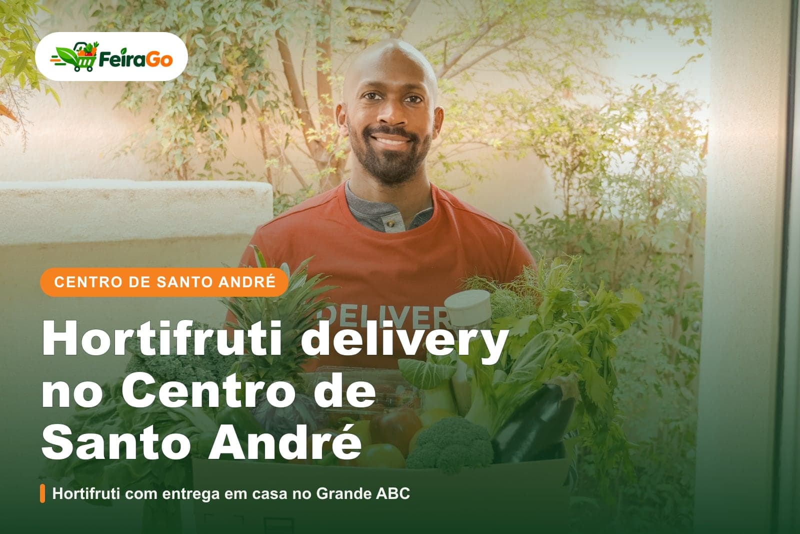 Entregador sorridente de camiseta vermelha segurando uma caixa cheia de verduras, legumes e frutas na porta de um prédio