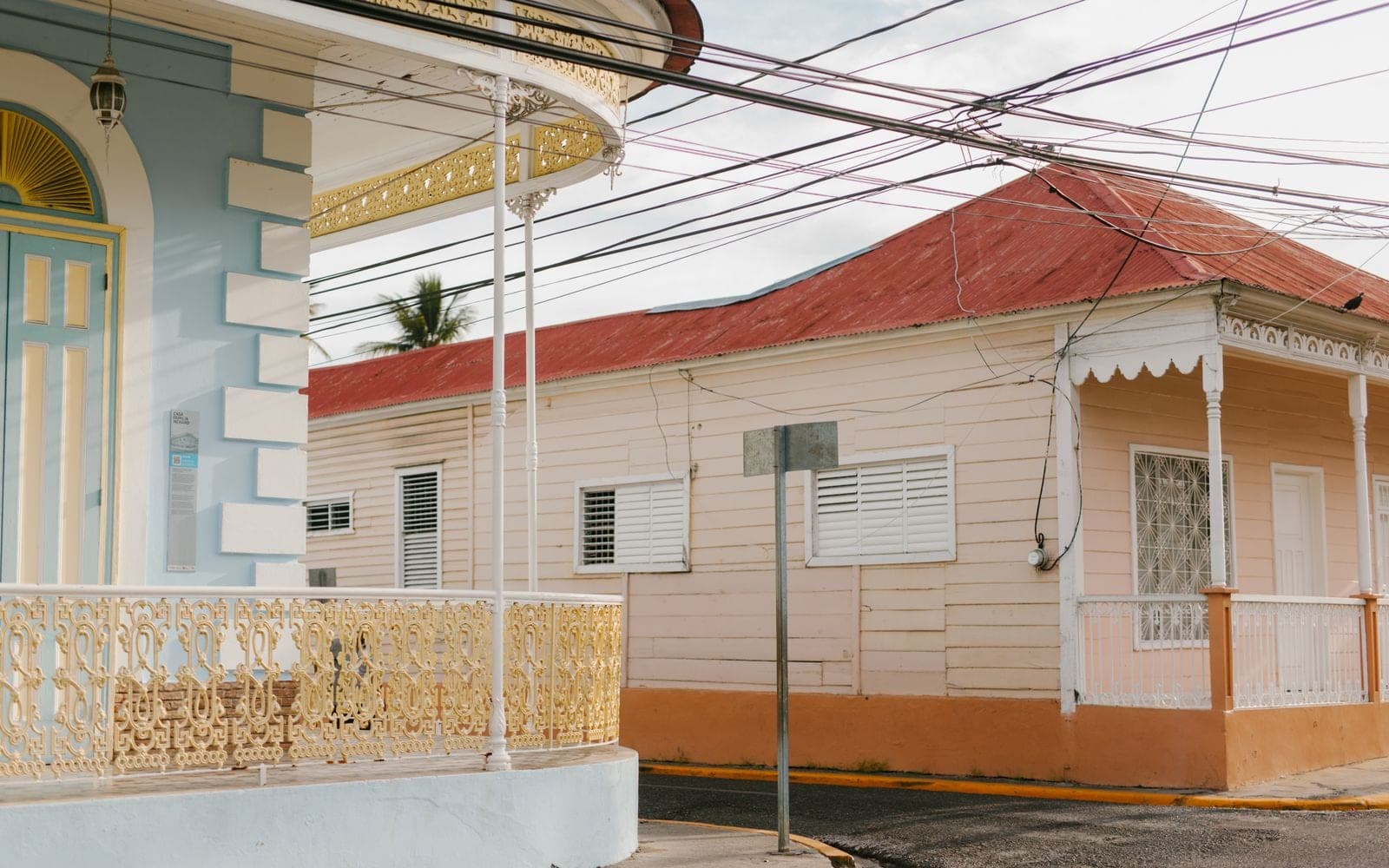 Casa antiga de esquina com fachada clara e telhado vermelho, com fiação na rua