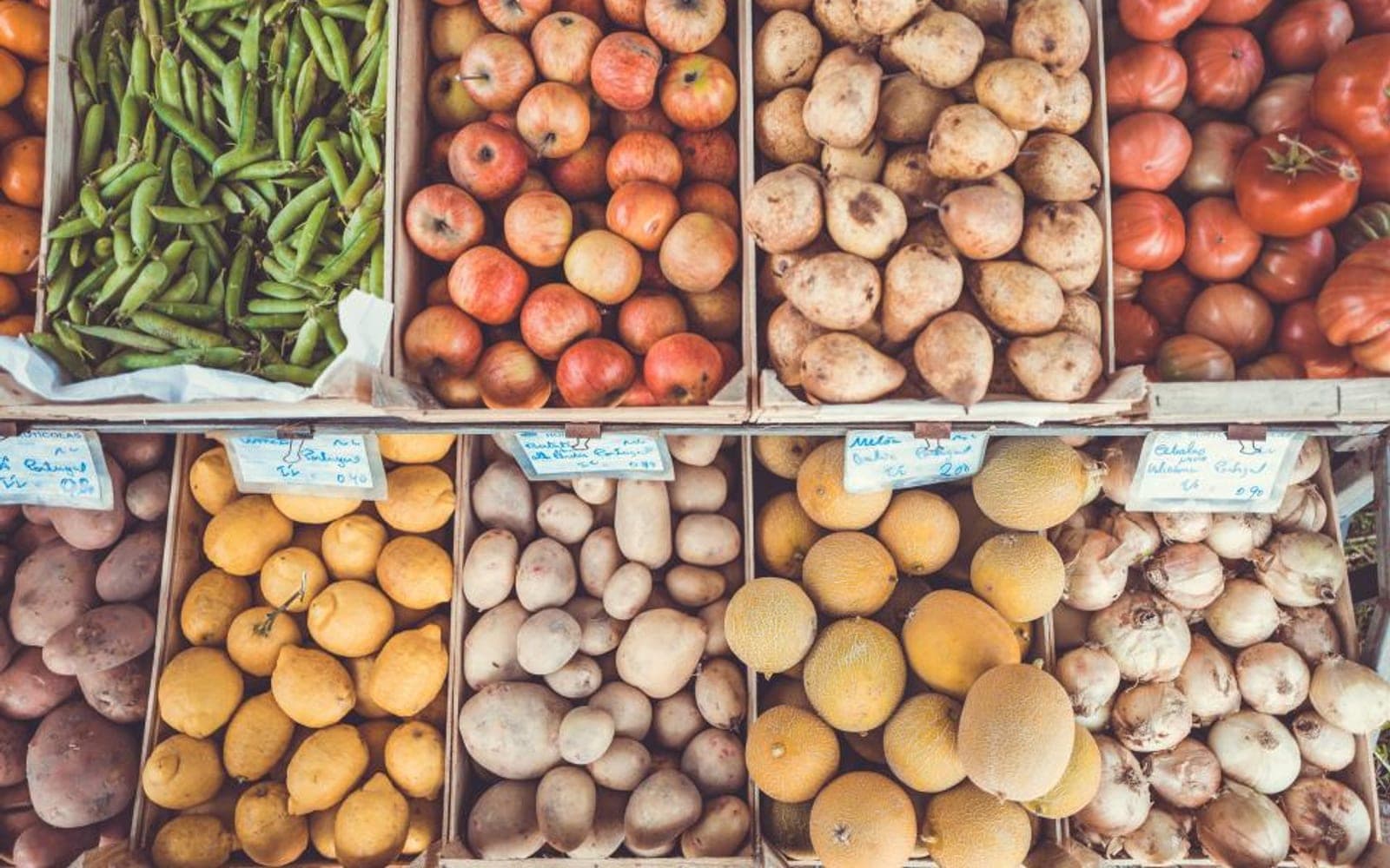 Caixas de feijão-vagem, maçãs, batatas e outros itens em uma banca