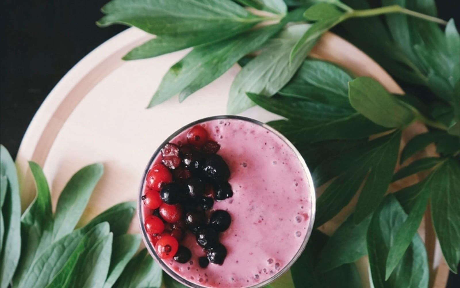 Copo de vitamina rosada com frutas vermelhas sobre folhas verdes