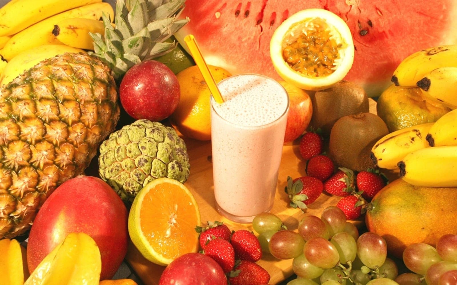 Abacaxi, maçãs, maracujá e uma vitamina cercados por frutas tropicais