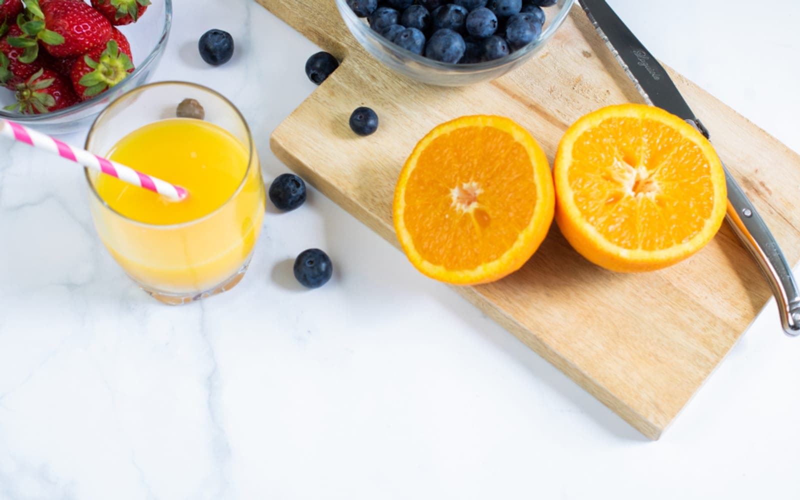 Copo de suco de laranja ao lado de laranjas cortadas e mirtilos sobre uma tábua