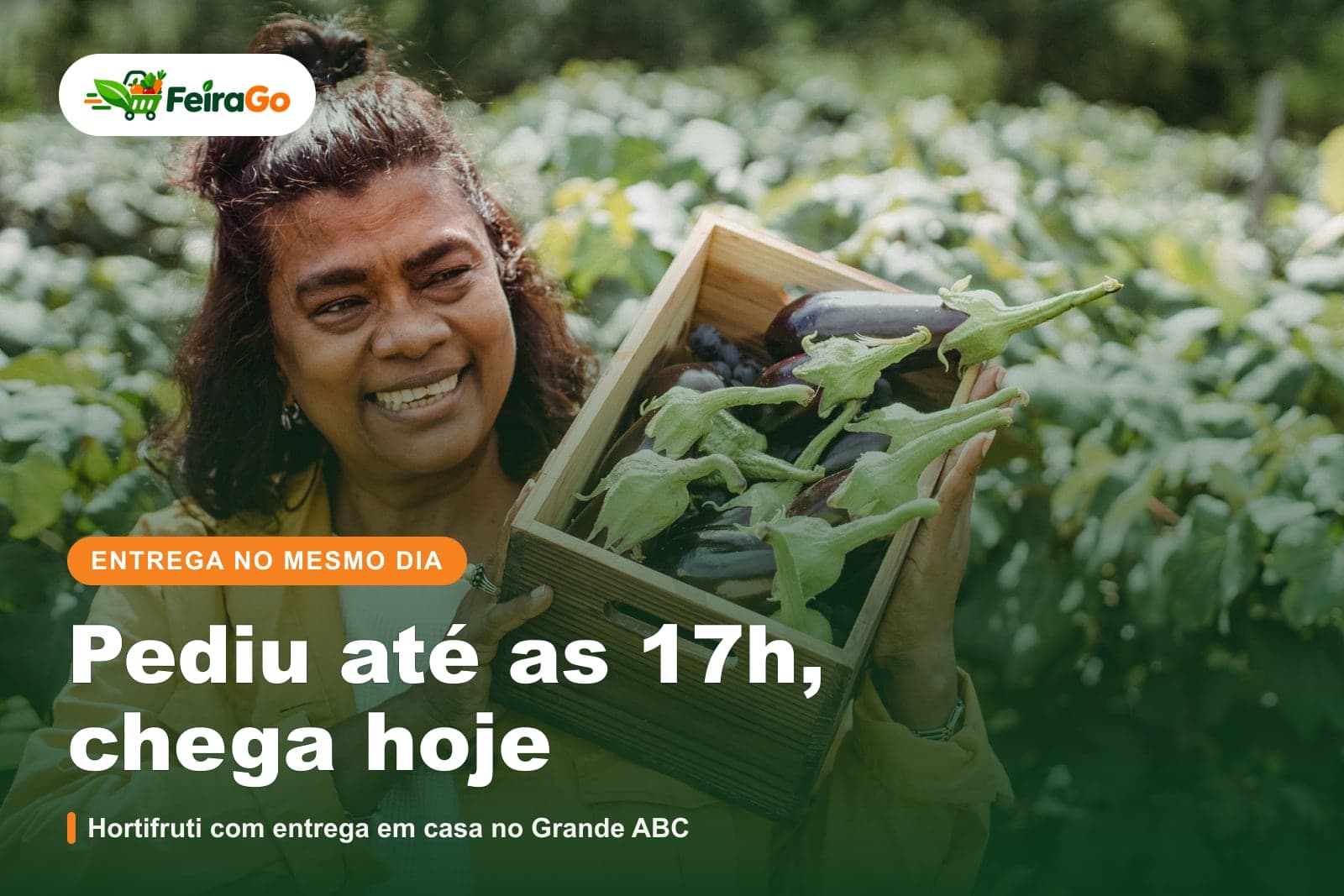 Mulher de jaqueta amarela sorrindo e segurando uma caixa de madeira com berinjelas recém-colhidas