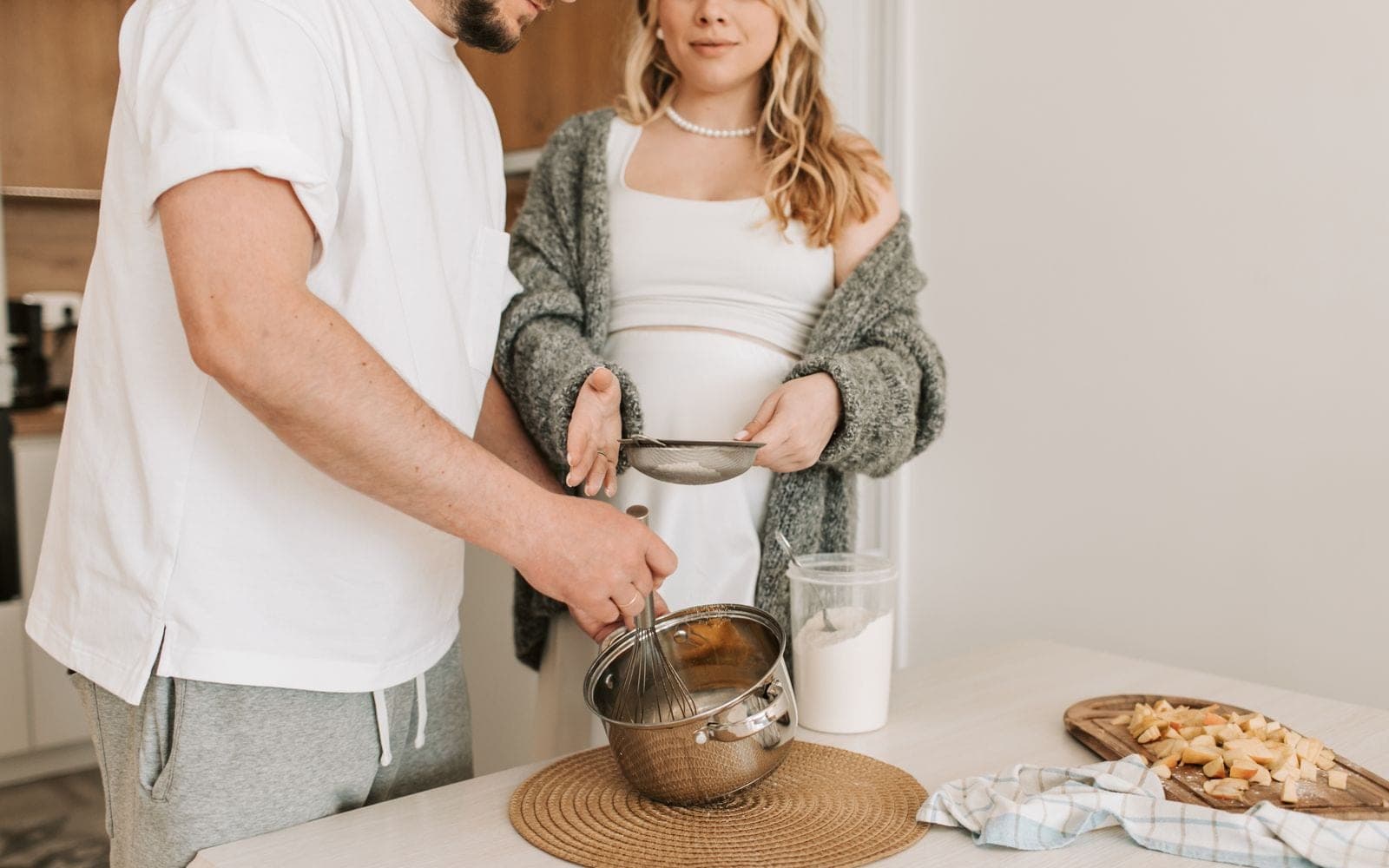 Casal prepara uma receita juntos na bancada de uma cozinha clara