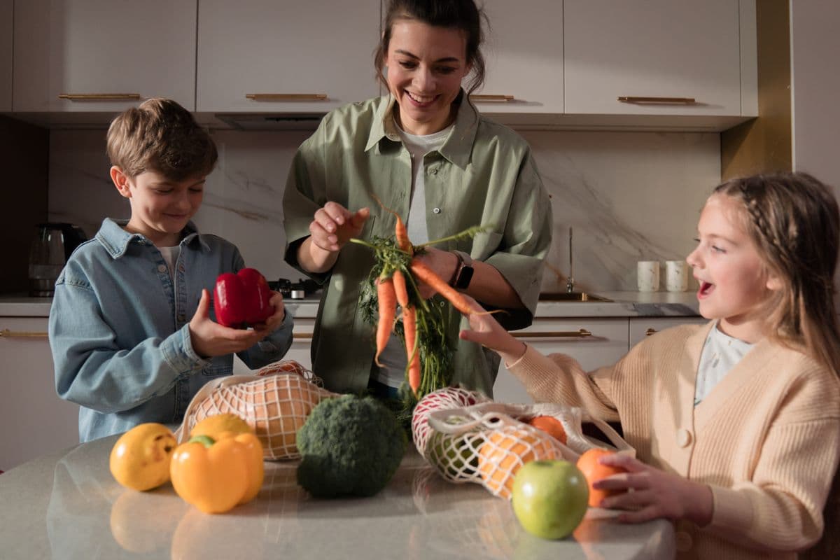 Mãe e filhos guardando frutas e legumes na cozinha