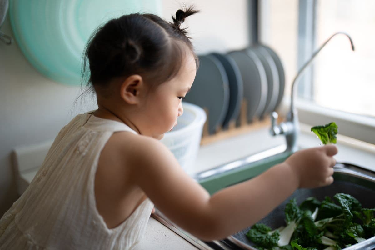 Criança pequena lavando folhas verdes na pia da cozinha