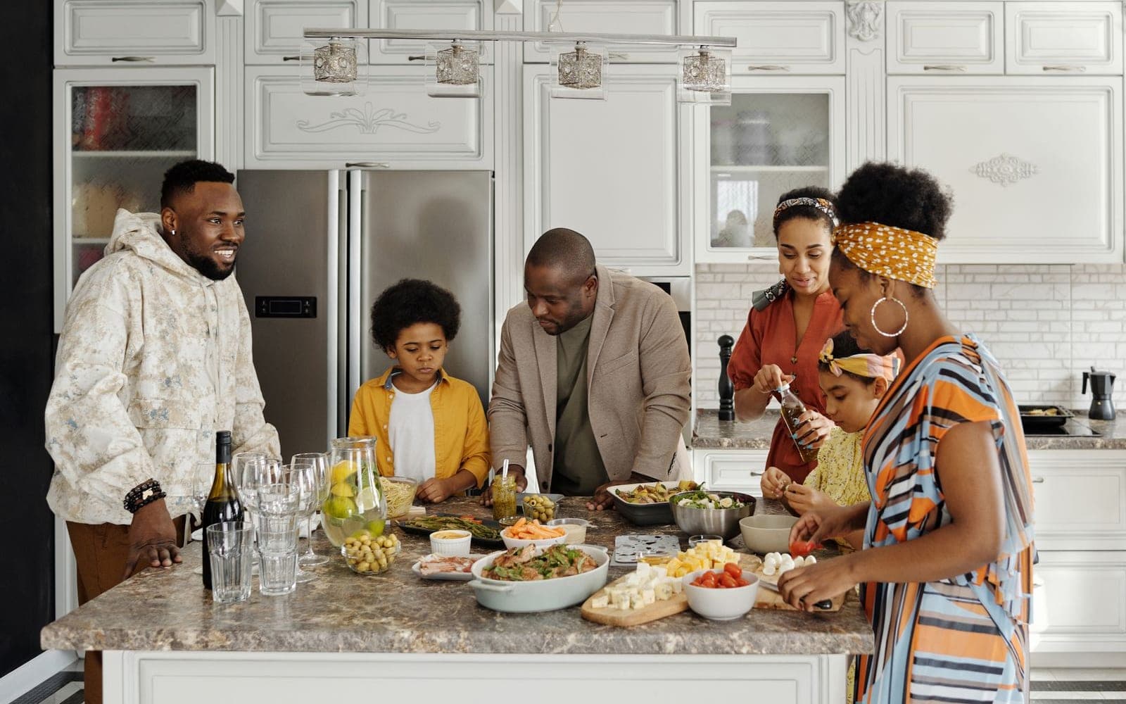 Família numerosa cozinhando junto numa cozinha ampla, com pratos de salada sobre a mesa