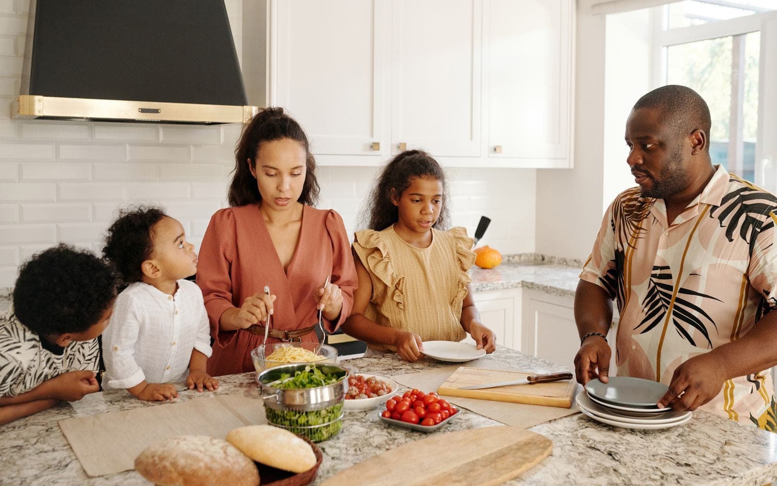 Casal e filhos preparando legumes e frutas numa bancada de cozinha cheia de ingredientes