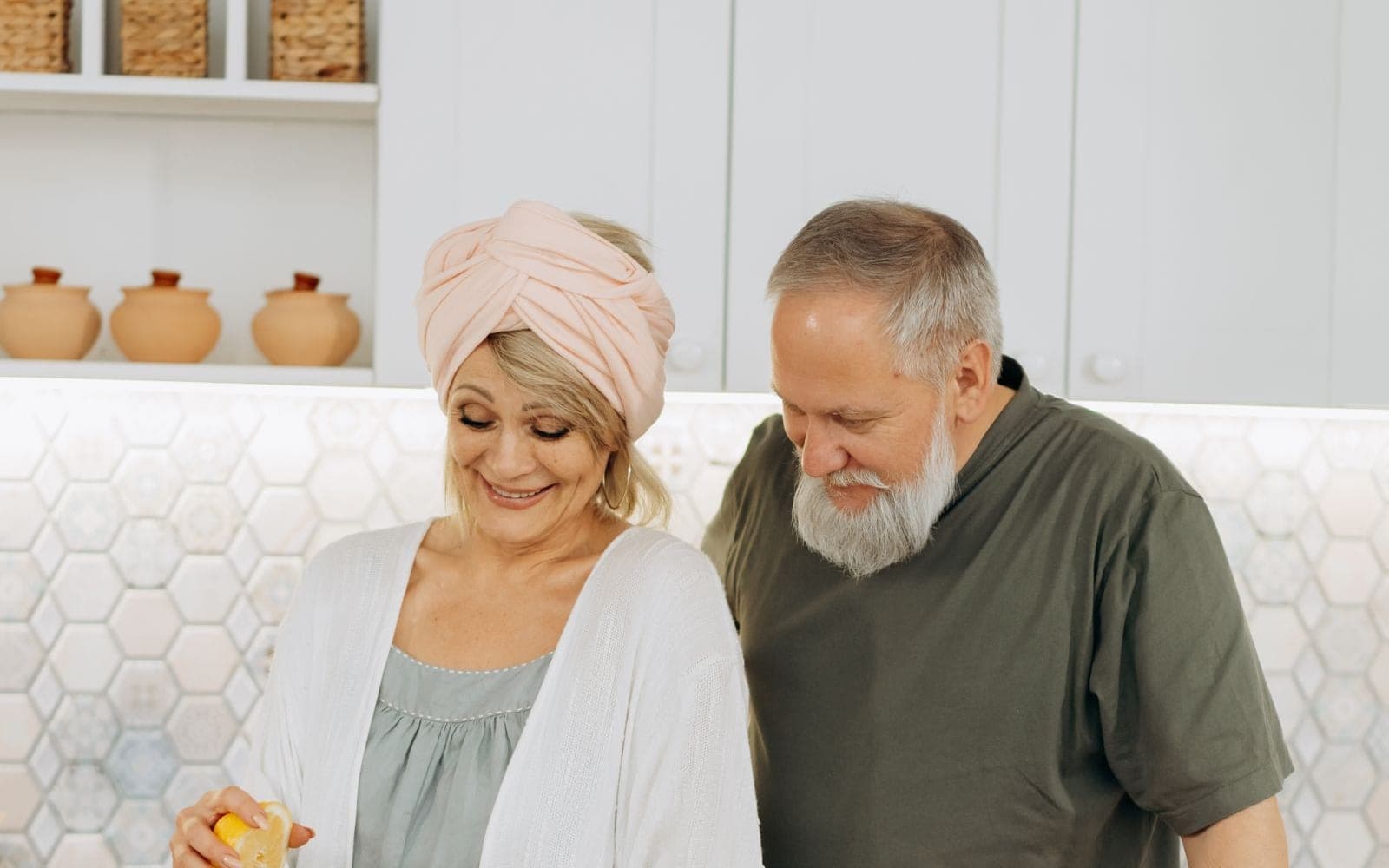Casal de idosos sorrindo na cozinha enquanto espreme laranjas