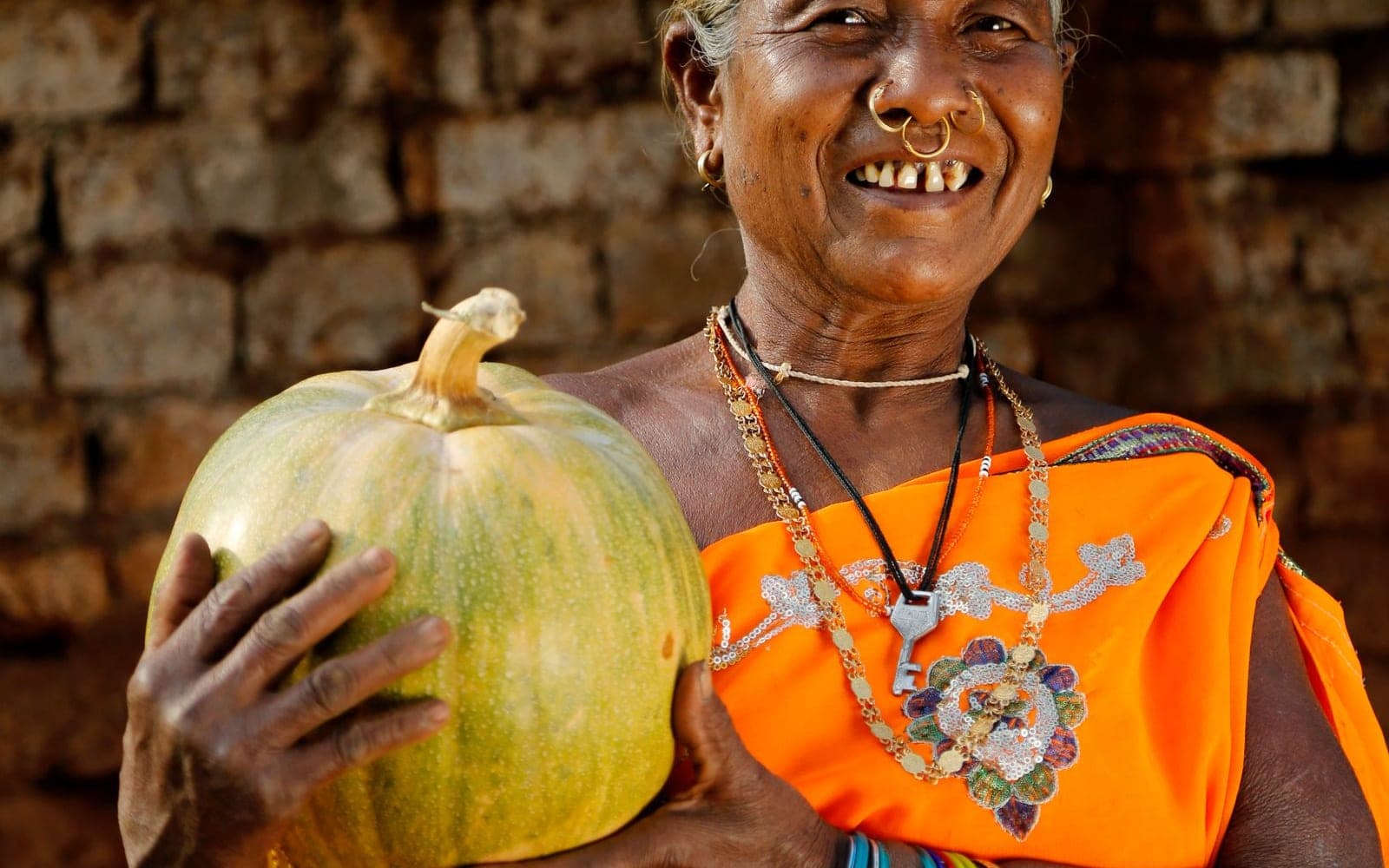 Senhora sorridente em frente a um muro de pedra segurando uma abóbora grande