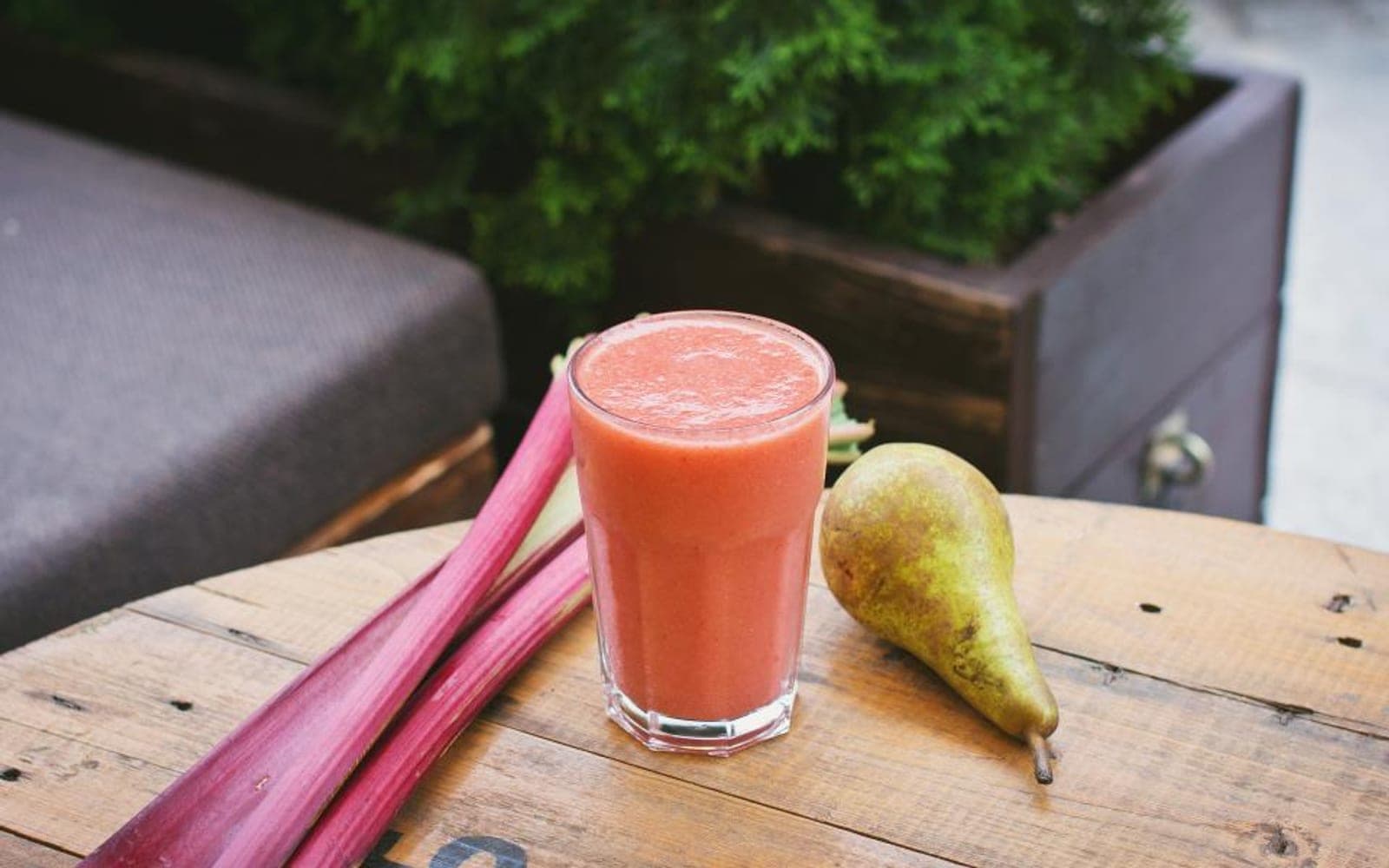 Copo de suco rosado ao lado de talos de ruibarbo e uma pera sobre um barril de madeira