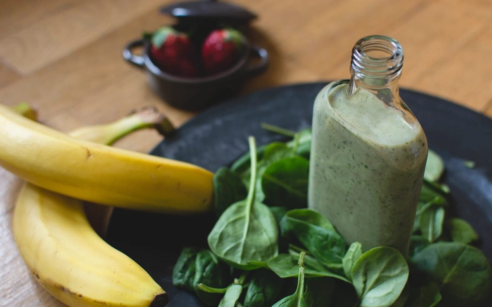 Garrafa de vitamina verde ao lado de bananas e folhas de espinafre
