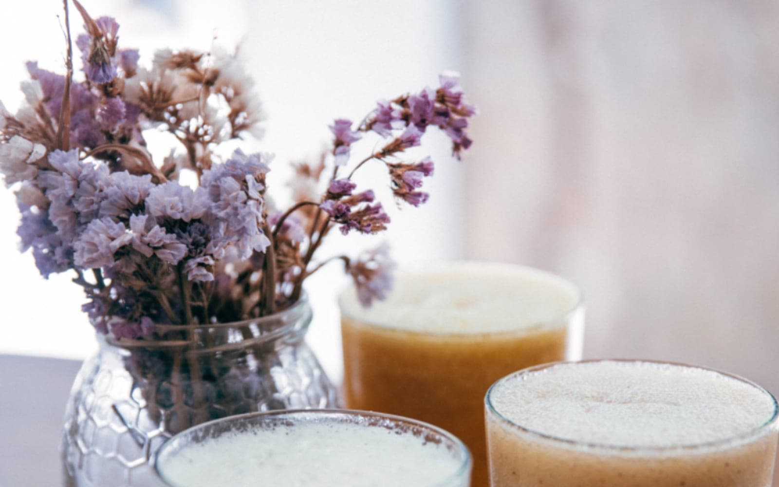 Dois copos de vitamina cremosa ao lado de um vaso com flores secas