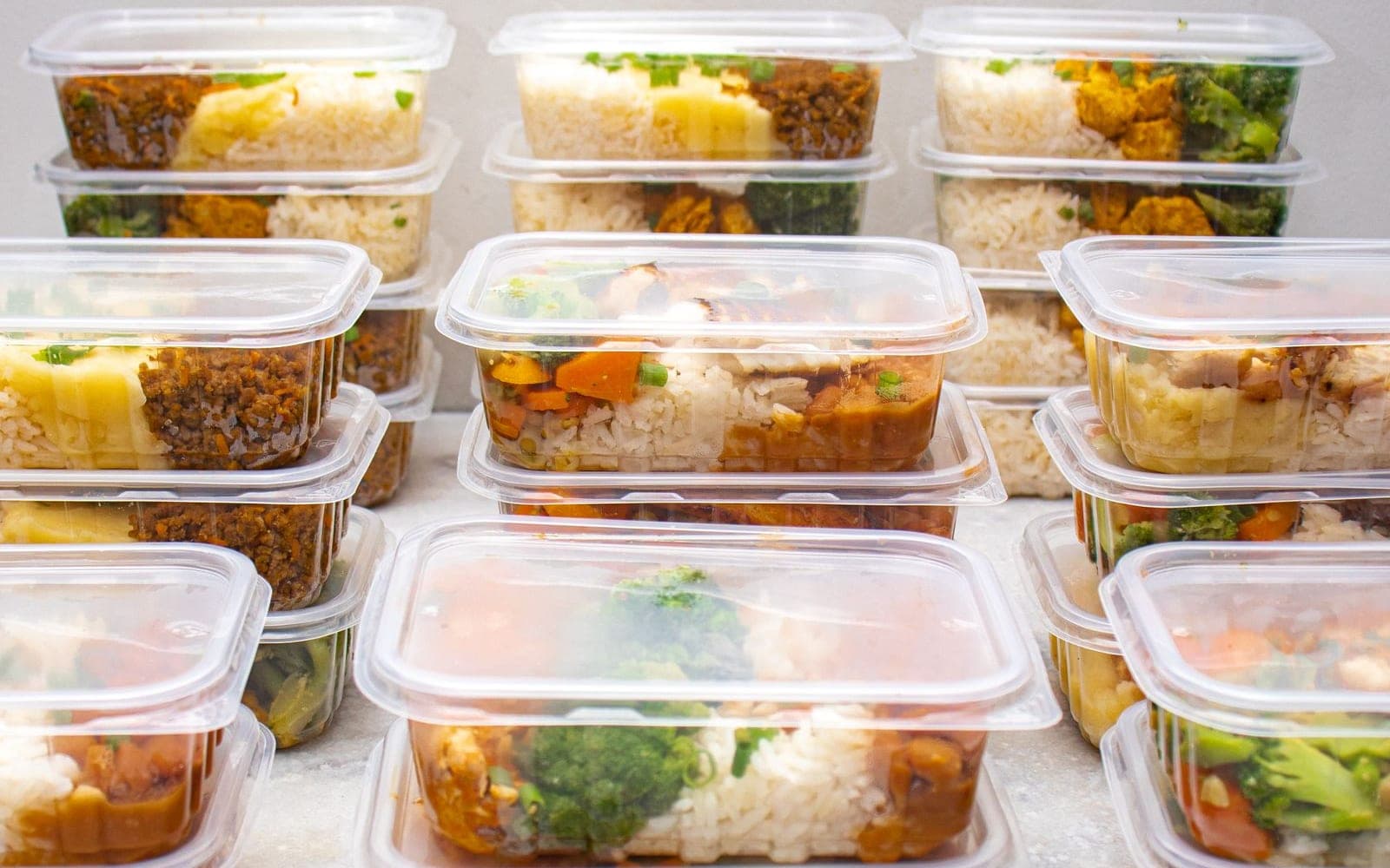 Várias marmitas transparentes empilhadas com arroz, legumes e proteínas