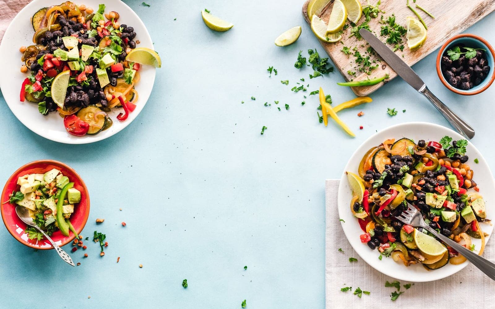 Duas saladas coloridas em pratos brancos sobre uma mesa azul clara com ervas e limão