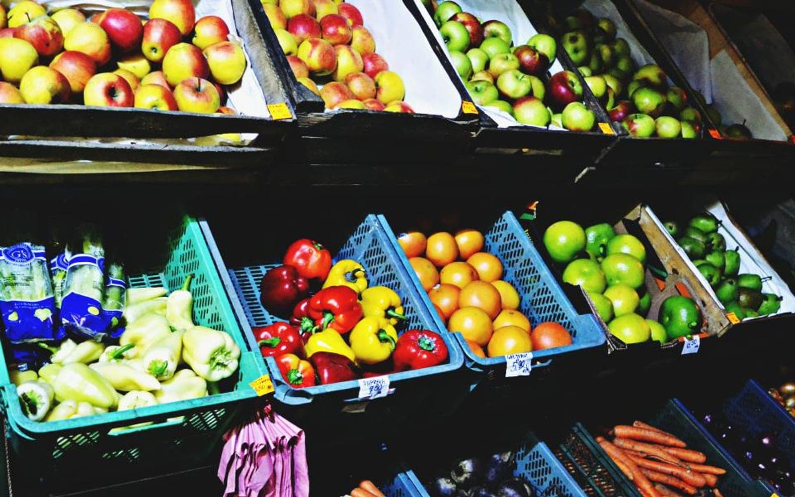 Prateleira com cestas de pimentões, maçãs, laranjas e cenouras