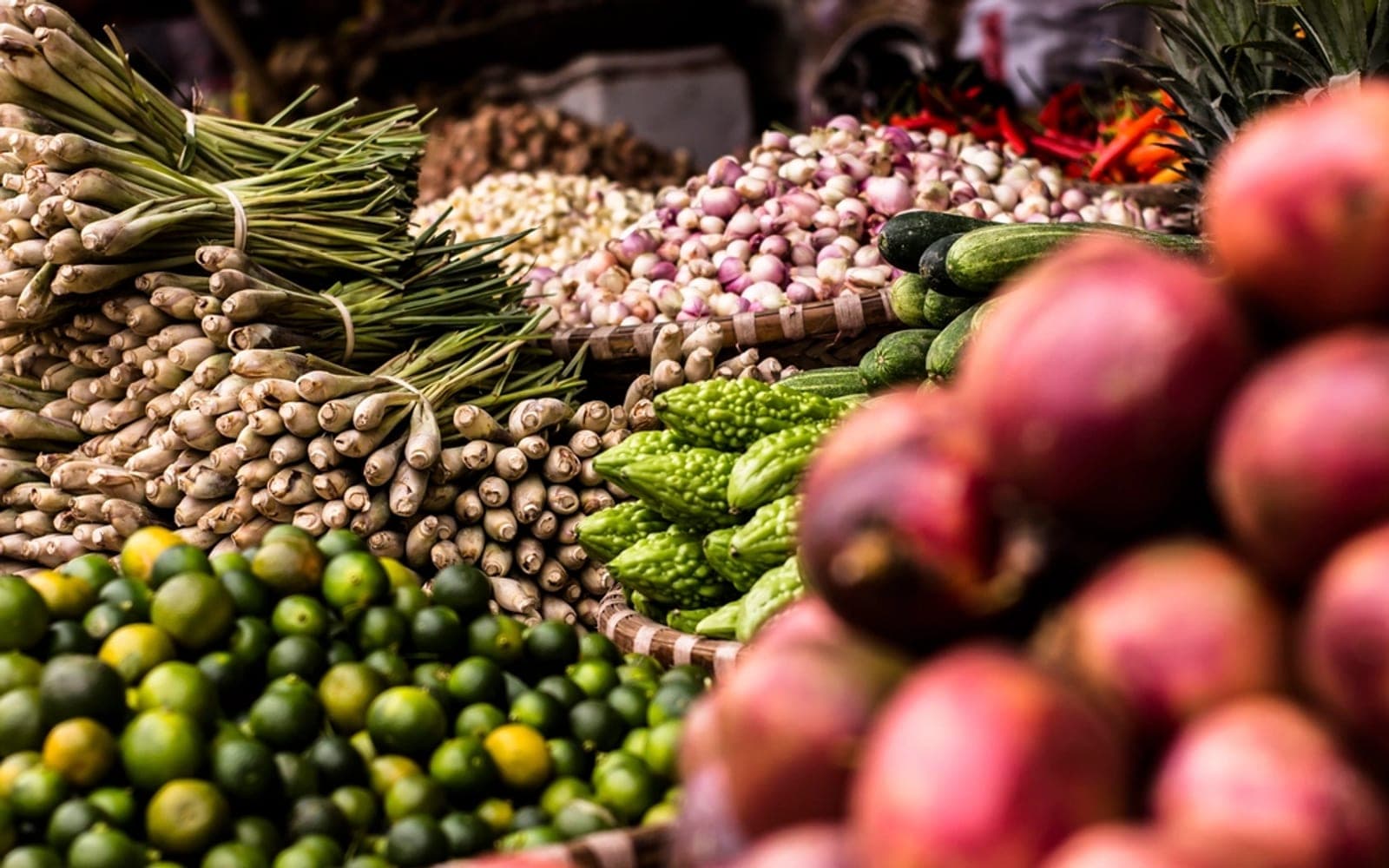Frutas vermelhas em primeiro plano diante de raízes, limões e verduras em uma banca