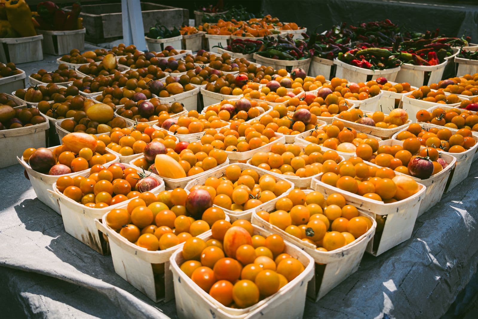 Cestinhas de madeira cheias de tomates-cereja amarelos e alaranjados numa banca