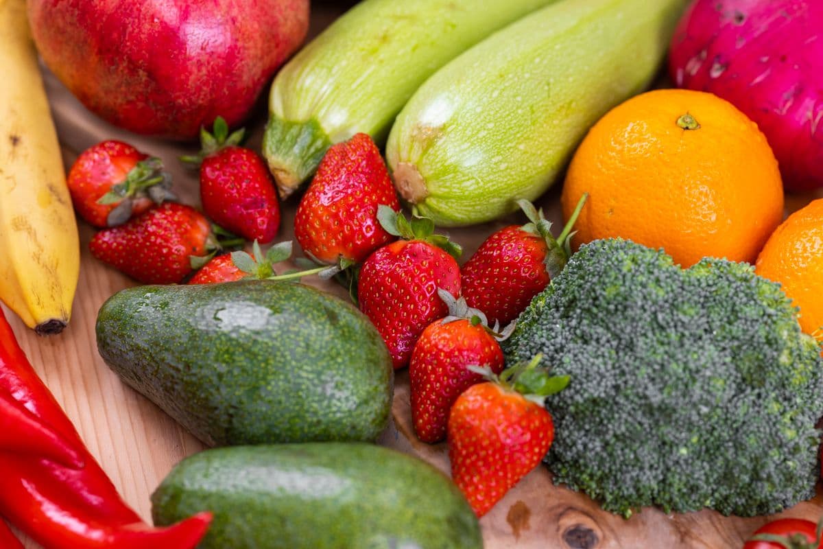 Morangos, abacate, abobrinha, laranja e brócolis em close sobre madeira
